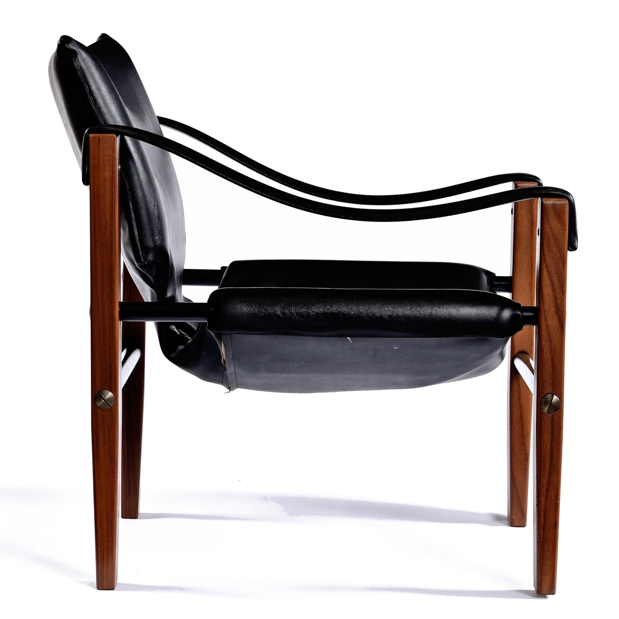 Classic and iconic Chelsea Safari Chair designed by Maurice Burke for Arkana Furniture in Scotland.  The original black leather contrasts perfectly with the reddish teak patina frame.   Black metal tube spanners create a solid stance and add to the