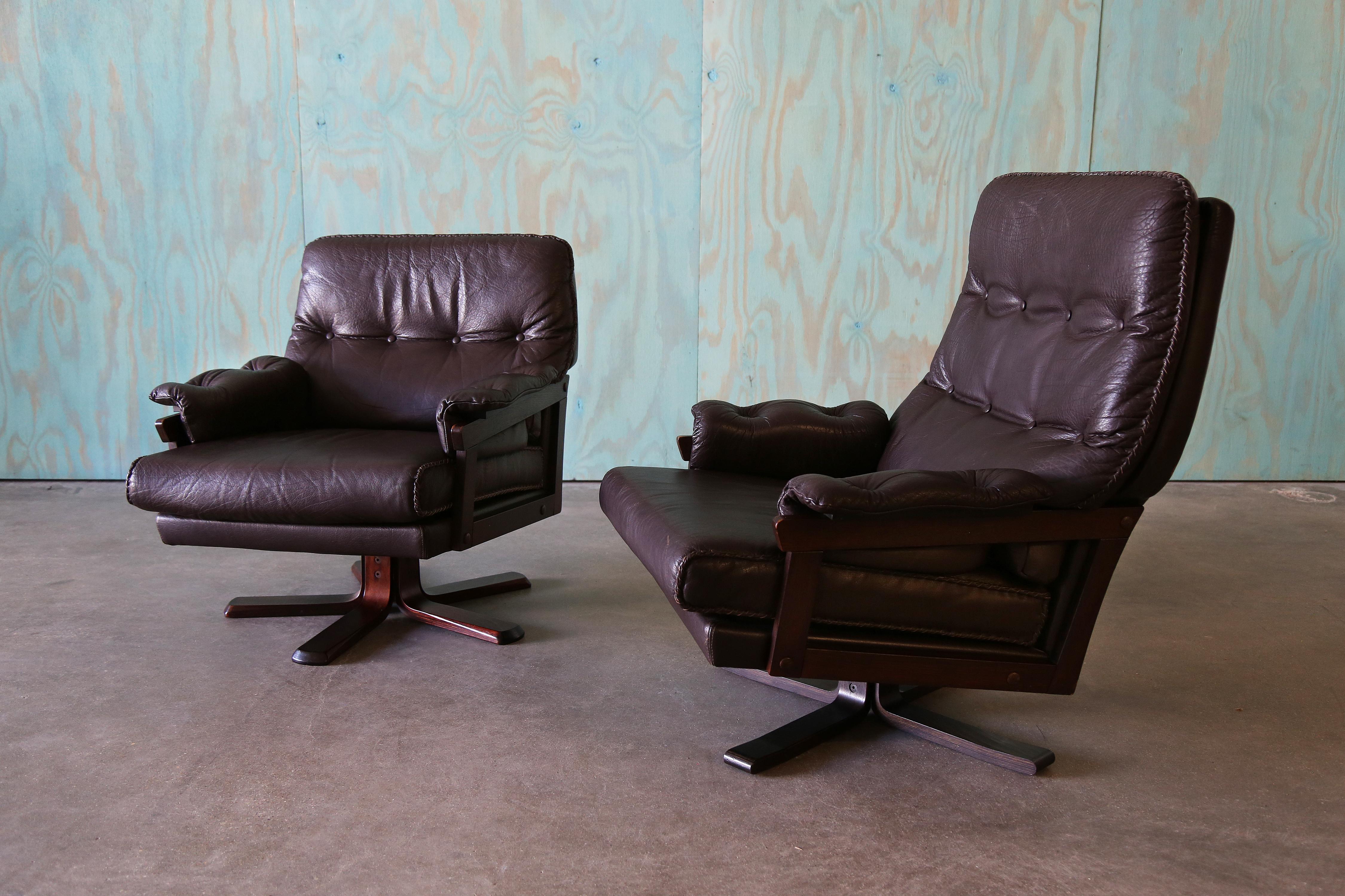 Una coppia di sedie da salotto in pelle cucite per lui e per lei degli anni '70 di Arne Norrell. Basi in Wood con cuciture esagerate. I braccioli in legno aperti e fluttuanti aggiungono un elemento di design. Queste sedie sono facilmente girevoli a