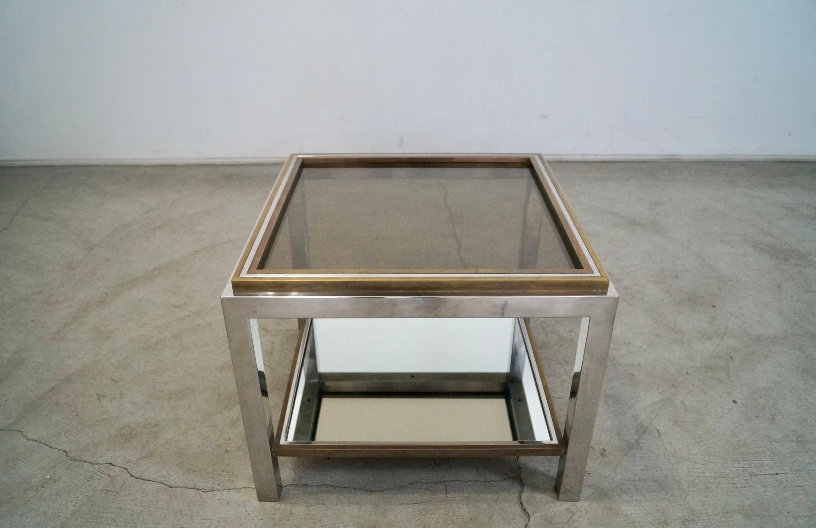 Vintage 1970's Midcentury Modern end table for sale. Has a chrome frame with brass trims on the top and bottom shelf. The bottom has a mirror glass insert and the top has a smoked dark glass. This is an original Jean Charles table, and is in the