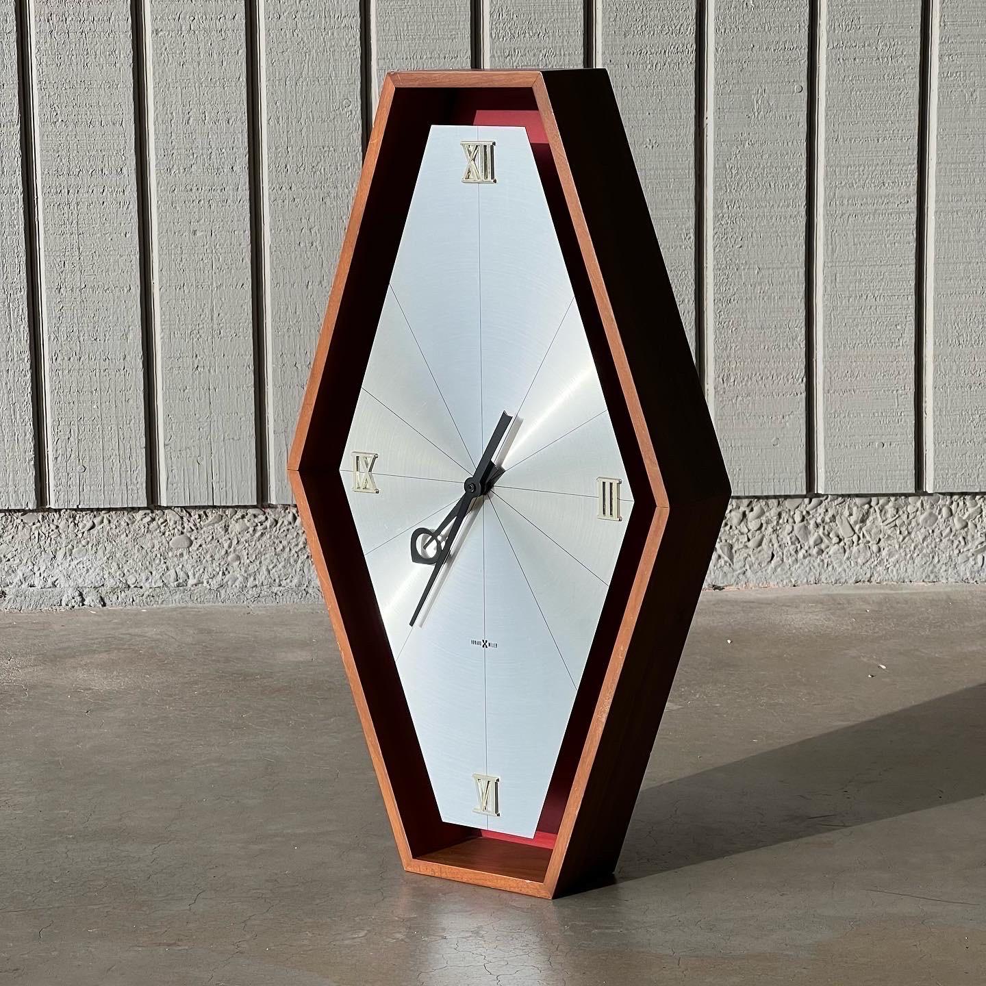 Arthur Umanoff for Howard Miller 1970s wall clock, model #588. Made of a walnut case, original red back, brushed aluminum clock face, brass Roman numerals and black hour and minute hands. In working condition and battery-powered. 11.75” wide x 20.5”