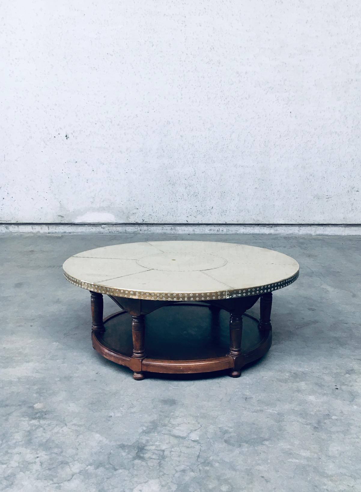 Vintage Artisan Design Brass Sheet covered round Coffee Table. Made in the 1970's. Wood constructed base with turned and carved legs. Brass sheets cover the top which are nailed. The brass top has wear marks from it's use and age with a dent in the
