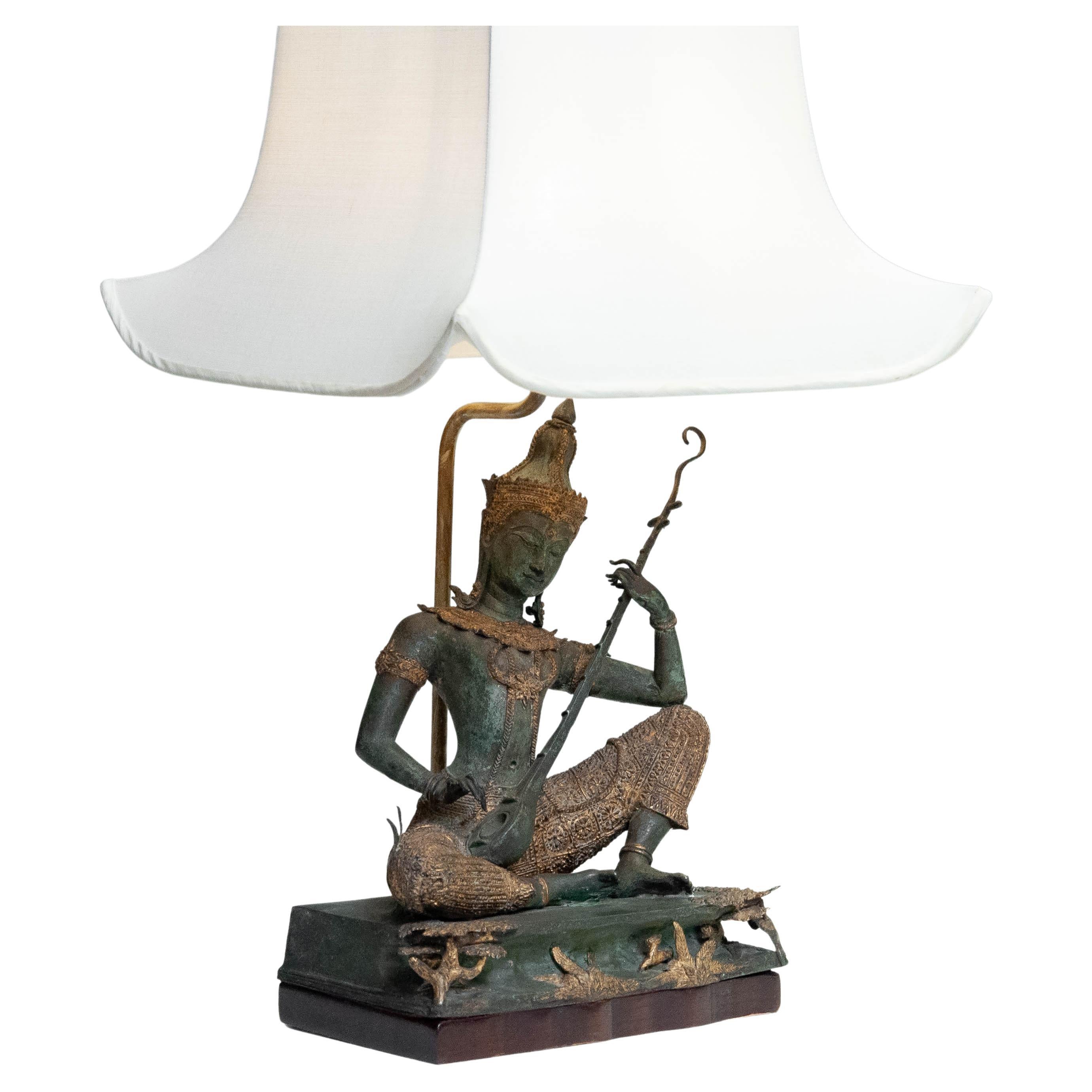 Beautiful and very decorative table lamp from Thailand with extremely detailed brass statue from Phra Aphai Mani from the 1970s. Playing the Jakhee ( three stringed guitar ).

Sitting and playing music on top of the representation of the several