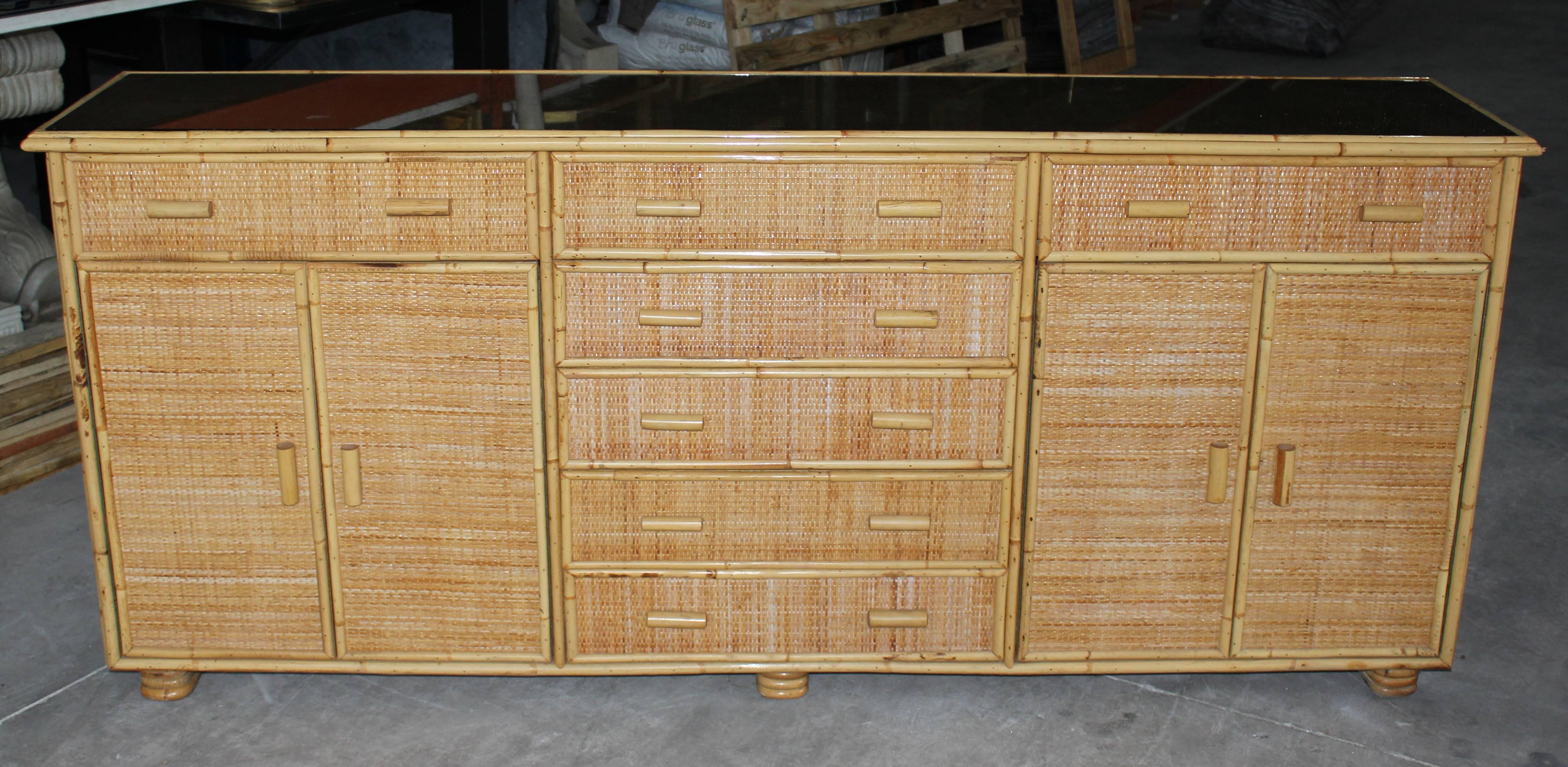 Seven bamboo and laced wicker drawers and two side cabinets topped with typical 1970s smoked glass.
   