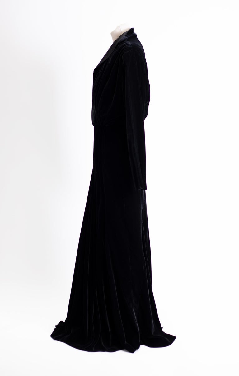 Voluptuous Runway dress, floor length in black silk velvet,  V-neck in grosgrain with small collar,  Long sleeves. slit opening in the back. with fish tail shaped draping from knee to floor back.

From 1970 starting as a traditional tailor’s shop,