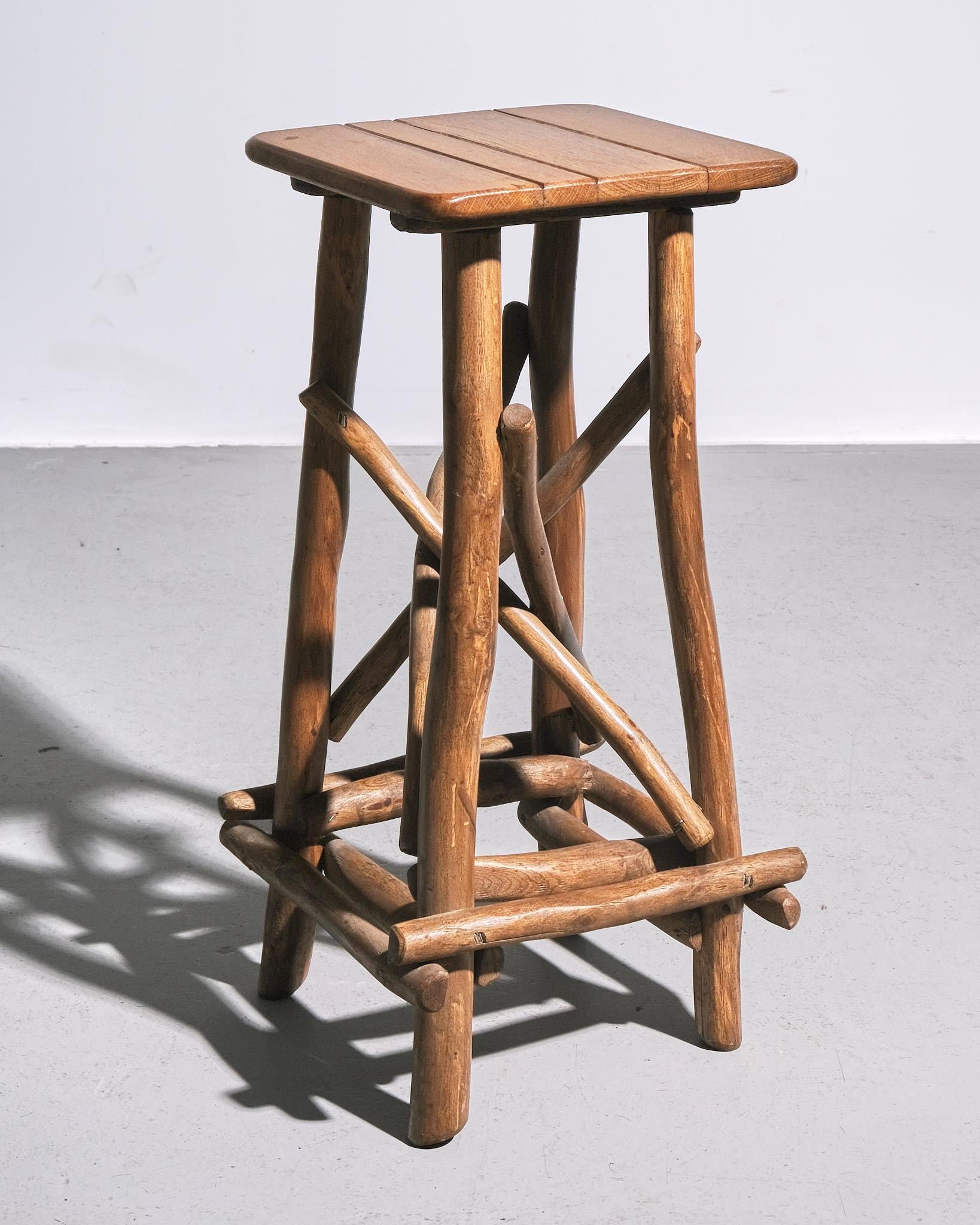 1970s Belgian Adirondack-style stool made of solid wood with a slatted square seat. The base features naturally shaped branch-like legs with intersecting supports for stability. Aged patina with visible wood grain. Sturdy and functional, suitable as