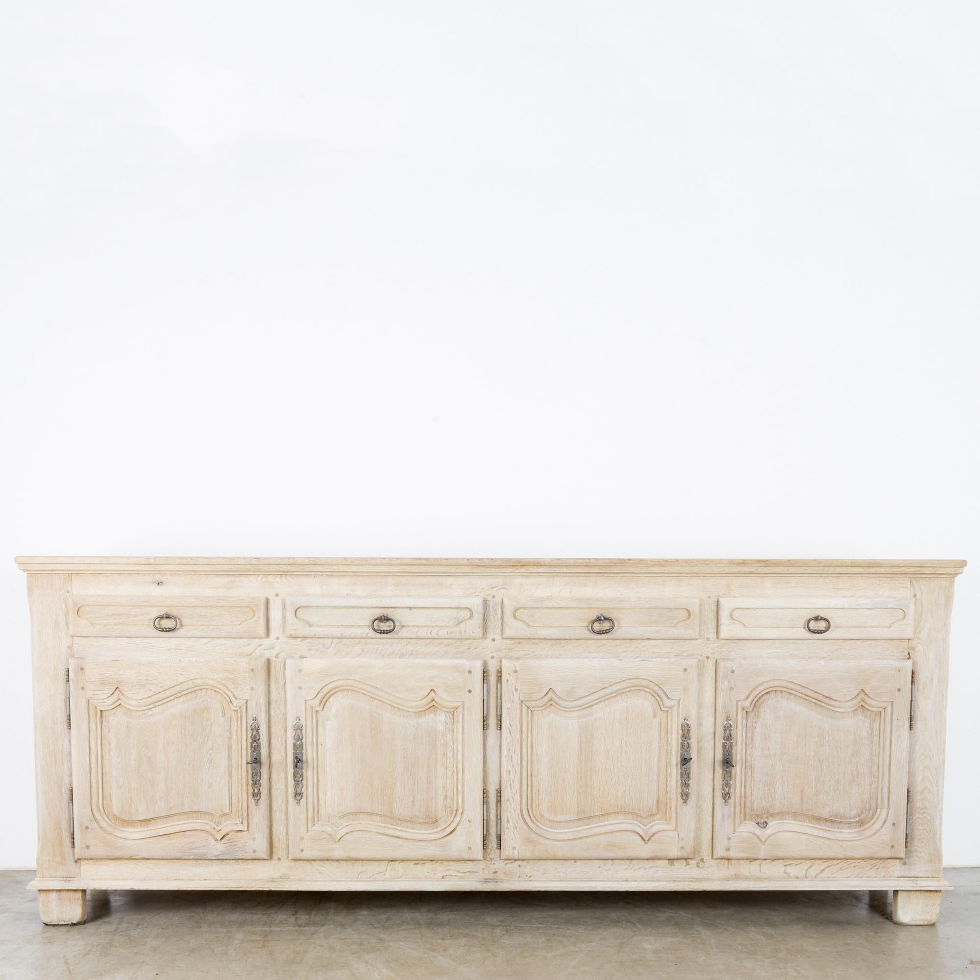 A bleached oak buffet from Belgium, circa 1970. At over eight feet long, this gorgeous buffet has storage galore in its quadruple drawers and double pair of cabinets. Raised on four feet, the undulating arches of the cabinet panels frame arabesque