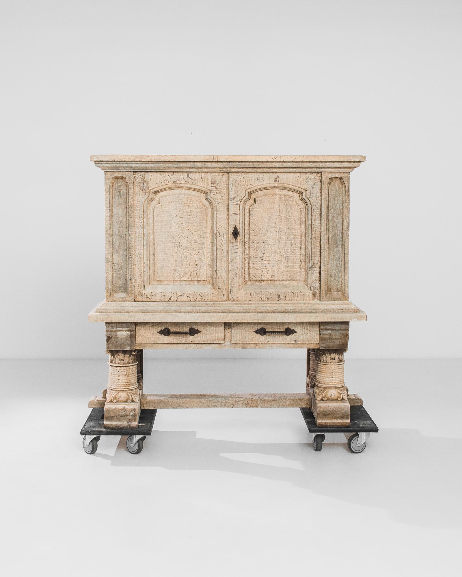 A bleached oak buffet from Belgium, produced circa 1970. Four thick, richly-carved legs with acanthus leaf motifs support a locking, double door, two shelf cabinet featuring two sliding drawers underneath. An arcade of recessed arches across the