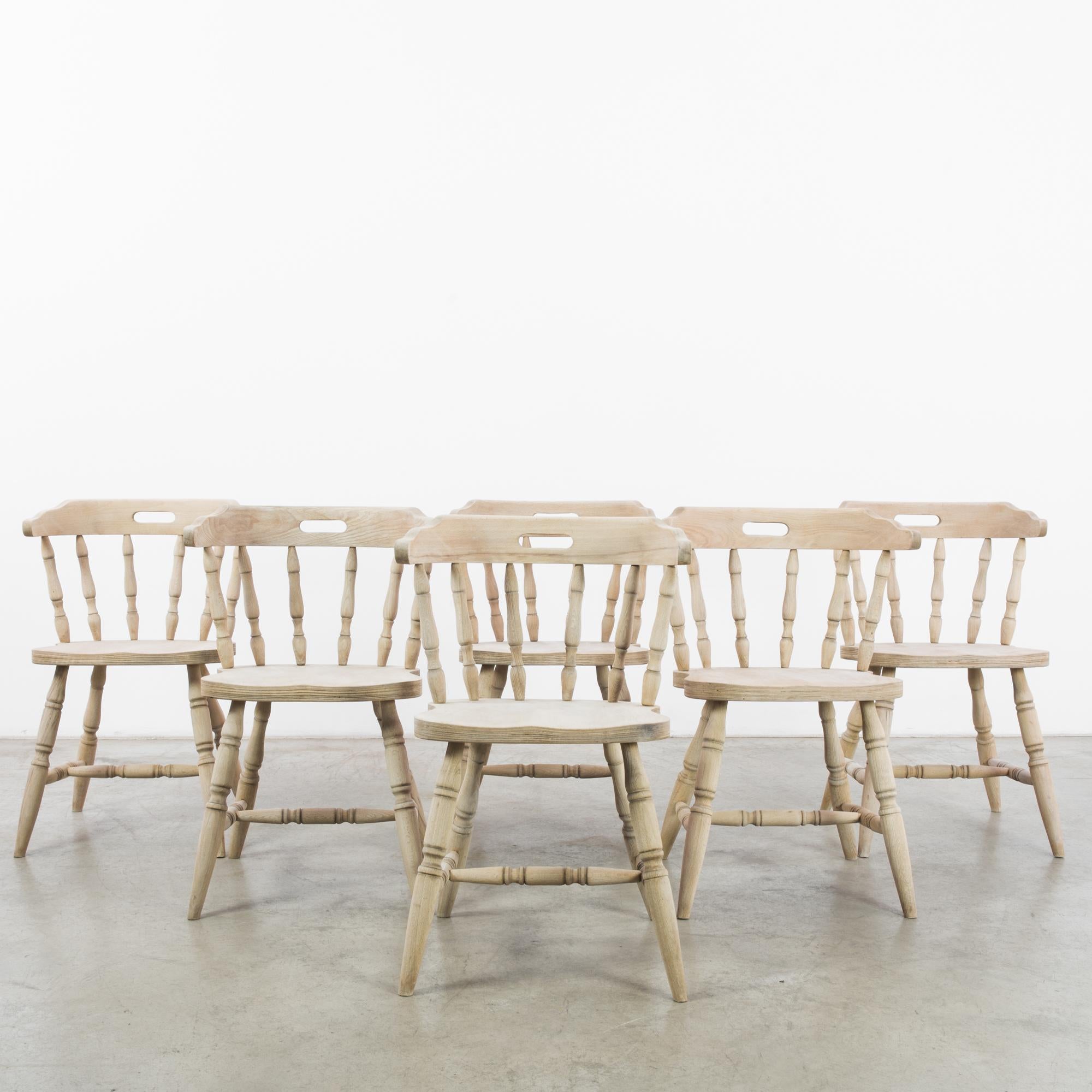 This set of six bleached oak dining chairs with turned splats and legs was made in Belgium, circa 1970. The splayed legs, contoured seats, and curved backrests give the chairs an expressive silhouette. Meticulously refurbished in our atelier for a