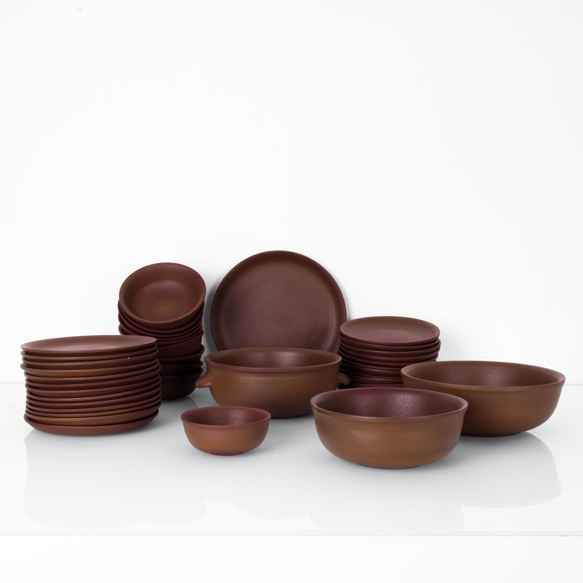 This 39-piece set of ceramic dinnerware includes dinner plates, side plates, bowls, and serving ware, in a beautiful earthy brown. It was made in Belgium, circa 1970. The simple and elegant forms allow the rich and warm tones of the pottery to stand