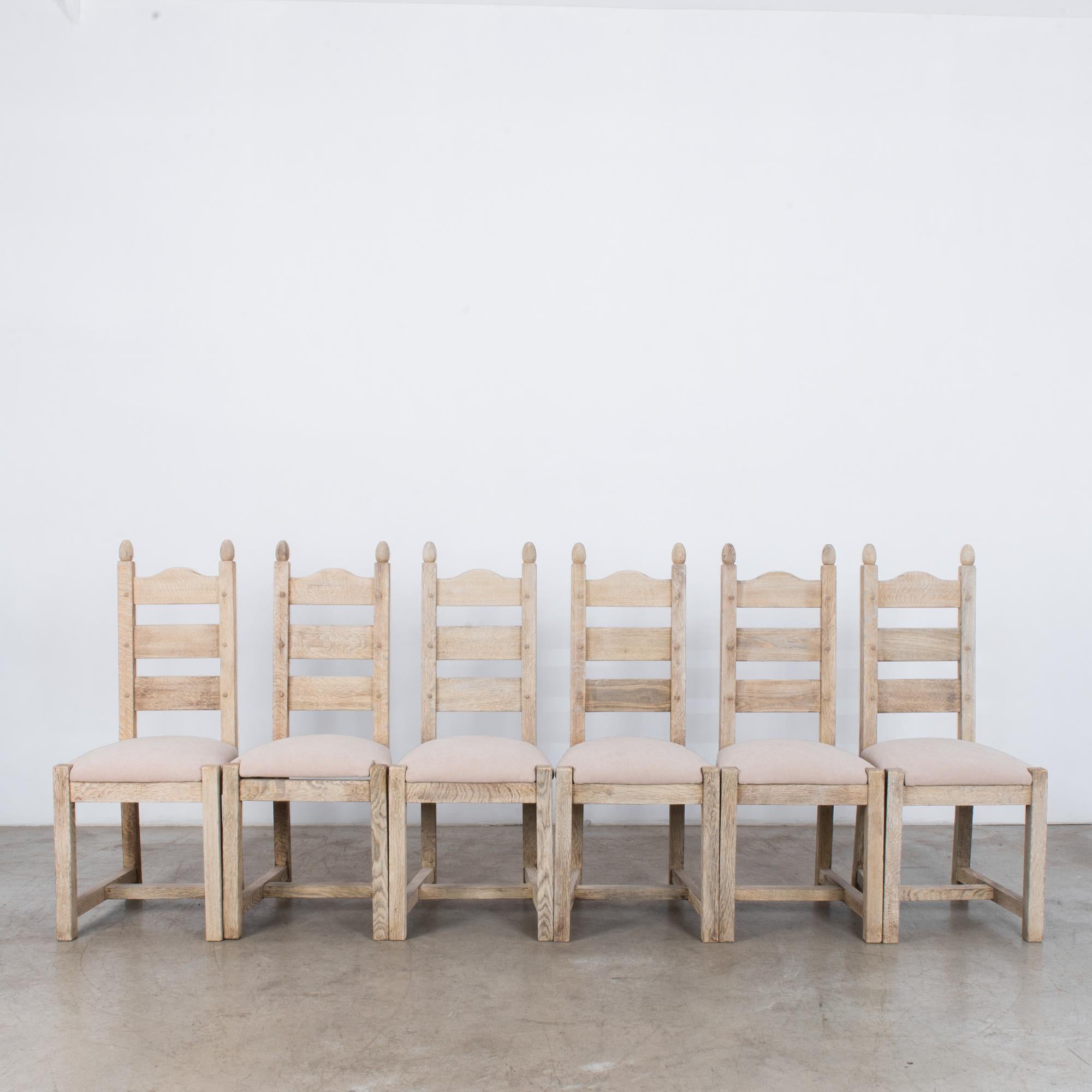 A set of six wooden dining chairs with upholstered seats from Belgium, circa 1970. A farmhouse shape, with four square legs joined by a strut, and a wooden backrest made of three slats. The seat is upholstered in a soft cream color. The light finish