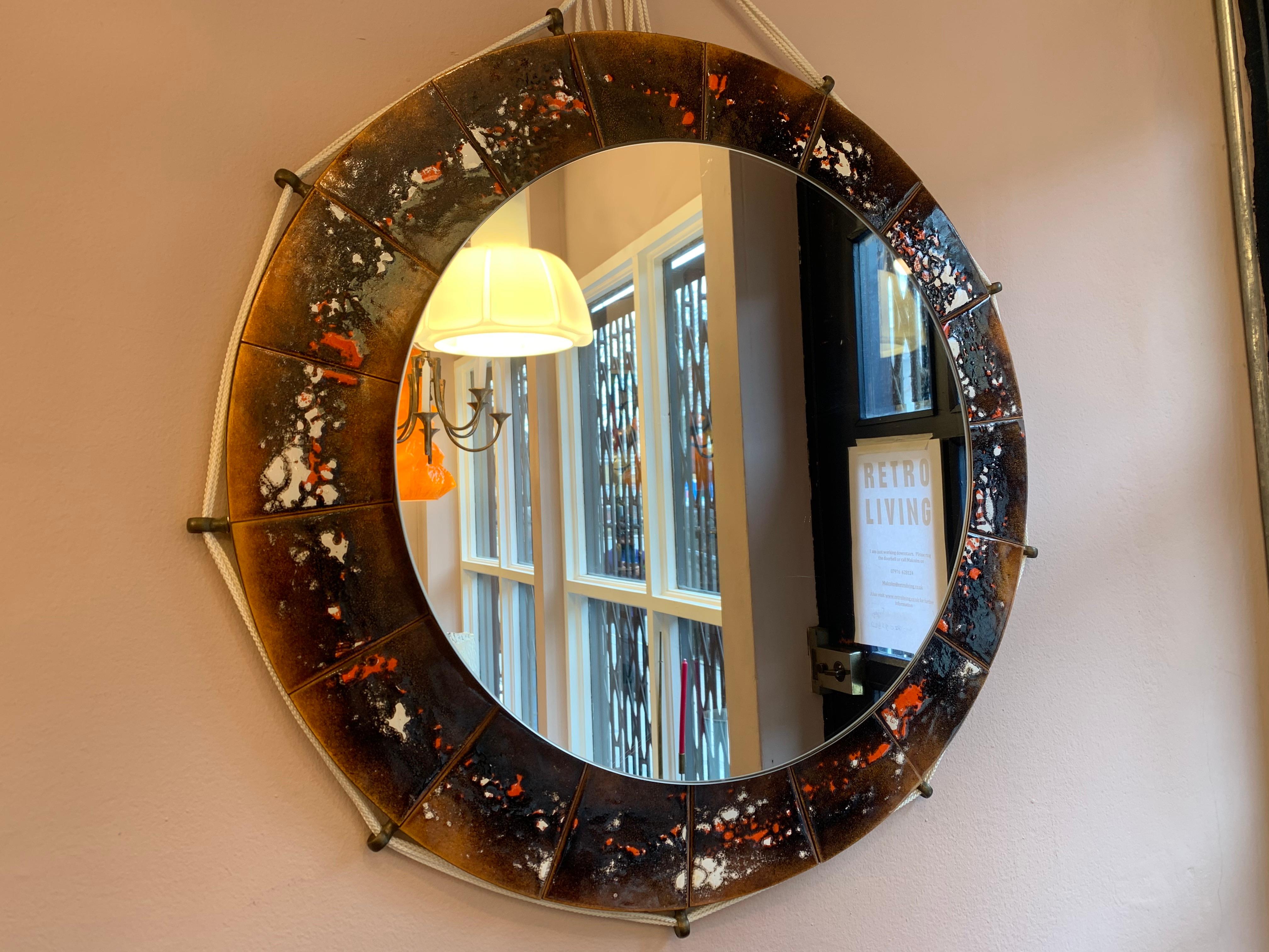 1970s Belgium, ceramic tiled, round, wall-mirror, with brass eye hooks, around its exterior with a white rope threaded through them. The rope connects to a round hook at the top which allows it to be easily hung on the wall. The round mirror stands