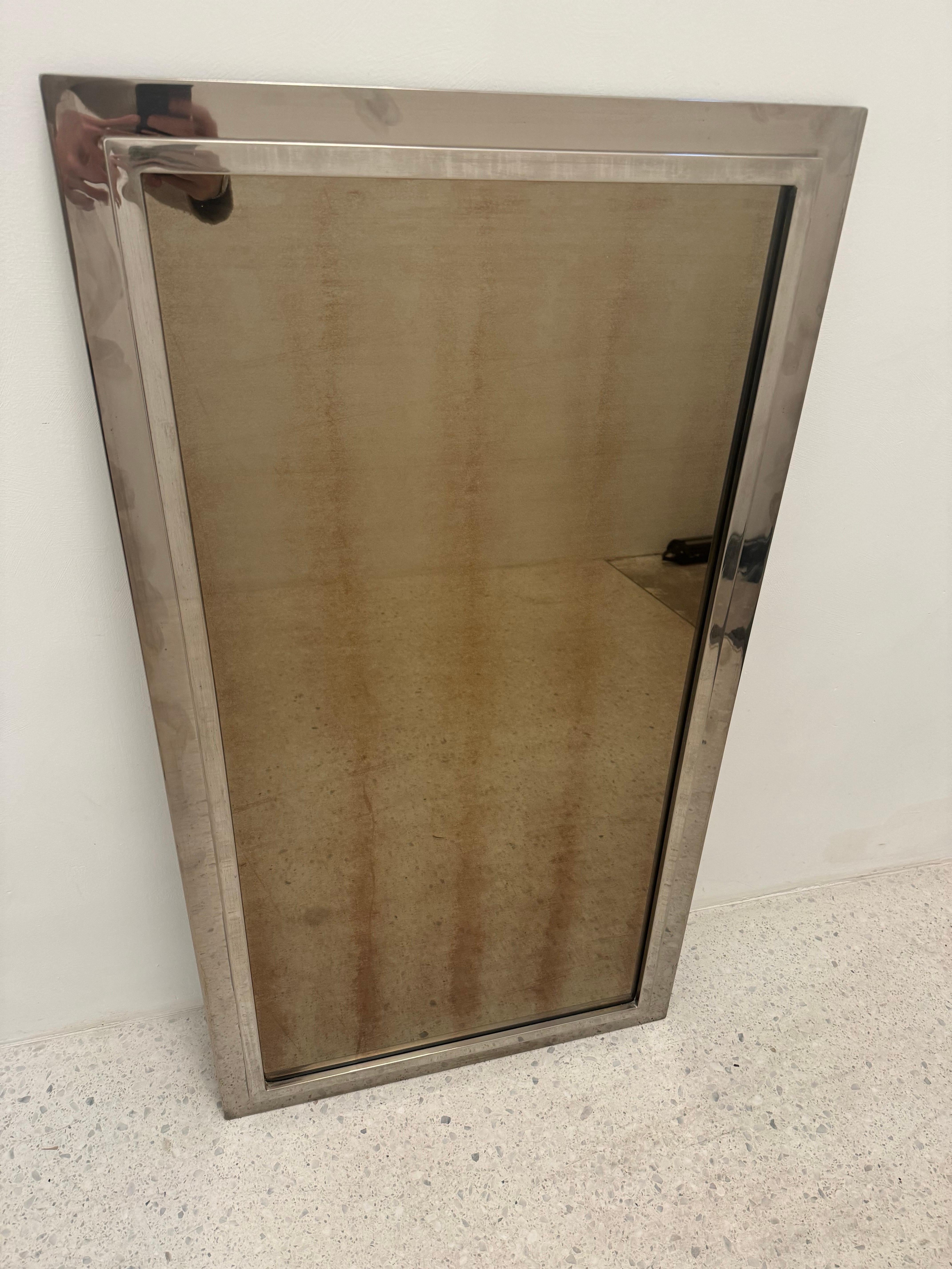 This bold and elegant 1970s wall mirror by Belgo Chrom captures the essence of the Hollywood Regency and Modernist design movements. Framed in polished chrome, the mirror features a deep bronze-tinted reflective surface, adding warmth,
