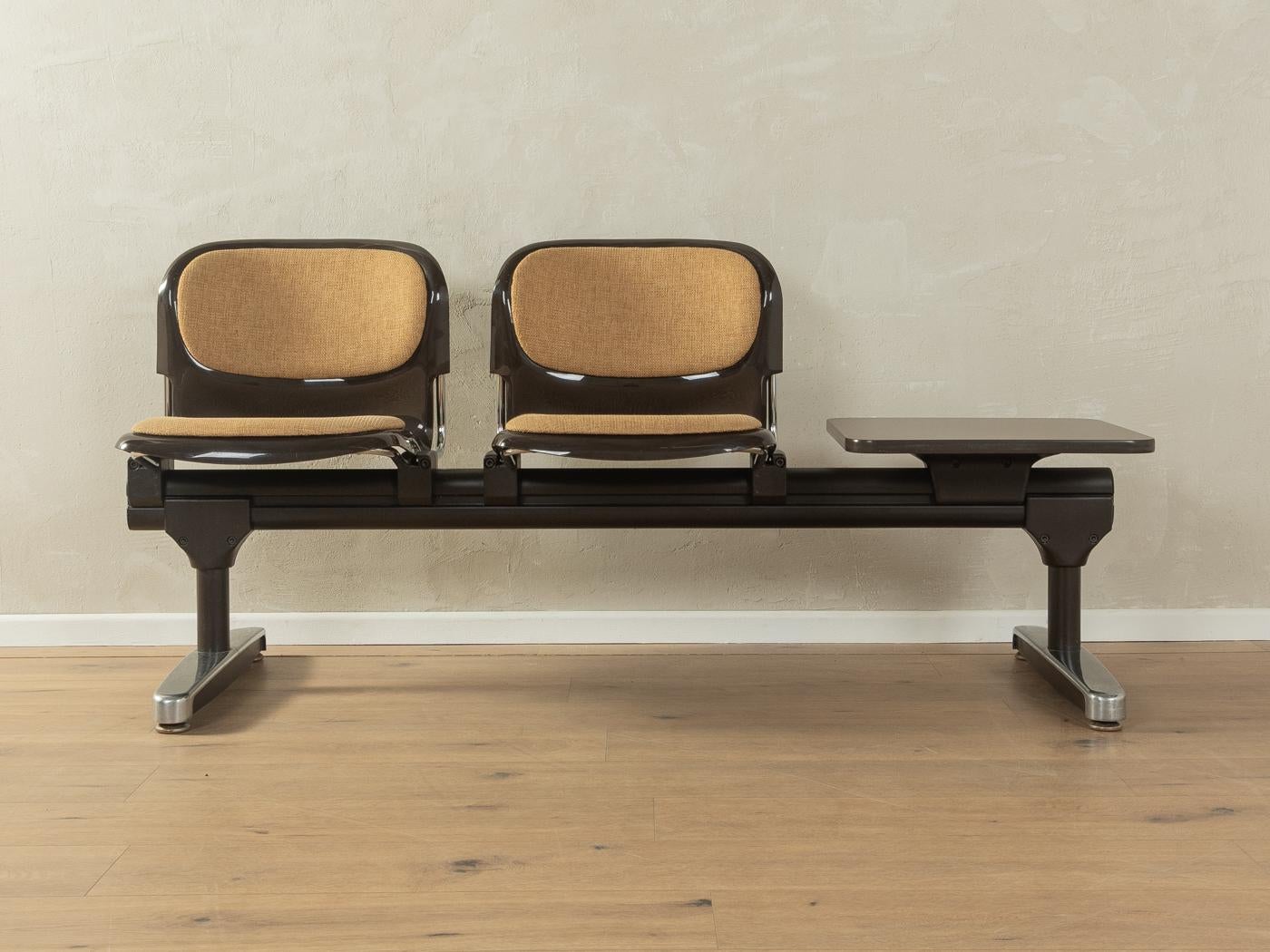Banco de espera clásico de los años 70. Estructura de acero y acero inoxidable de alta calidad con dos carcasas de asiento de plástico en marrón y tablero de mesa con revestimiento HPL original y borde de plástico en marrón. El tejido original se ha