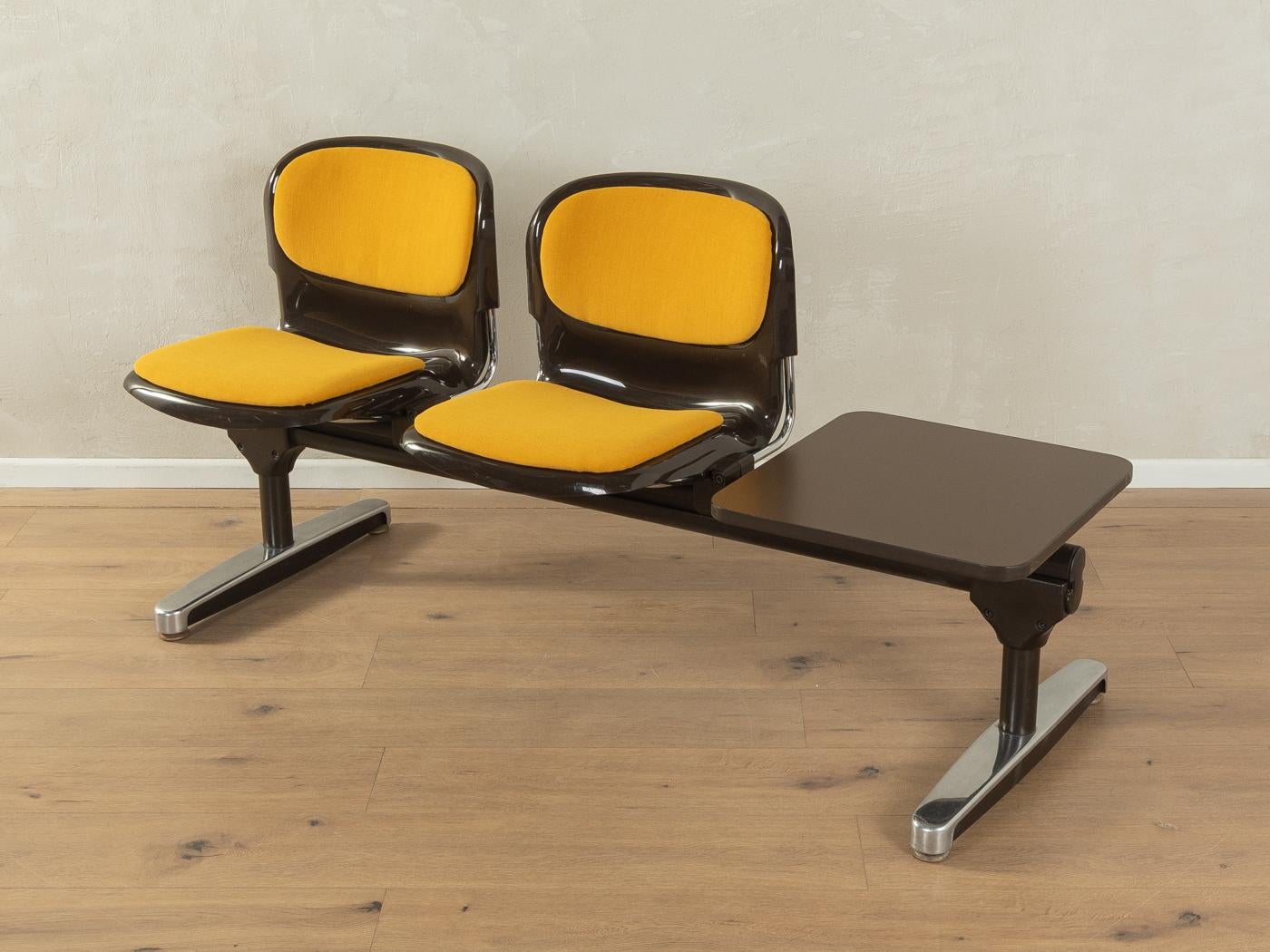 Banco de espera clásico de los años 70. Estructura de acero y acero inoxidable de alta calidad con dos carcasas de asiento de plástico en marrón un tablero de mesa con revestimiento HPL original y borde de plástico en marrón. Las carcasas de los