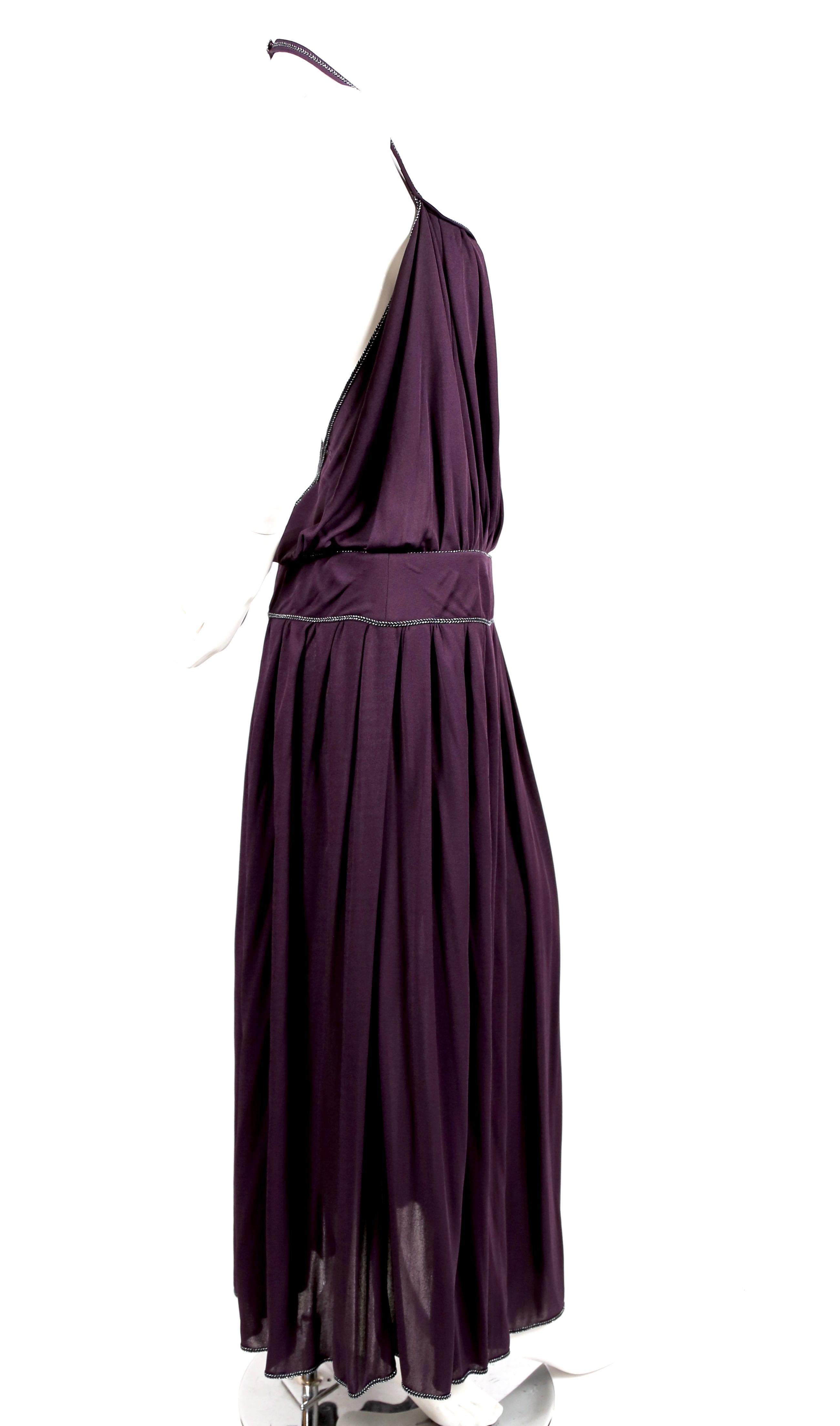 Purple viscose jersey gown with metallic silver toned trim and extra high thigh slit from Bill Gibb dating to the 1970's. Blouson bodice. Halter neckline with decorative button at back of neck. Dress is labeled a UK 12 (US 8) however this dress runs