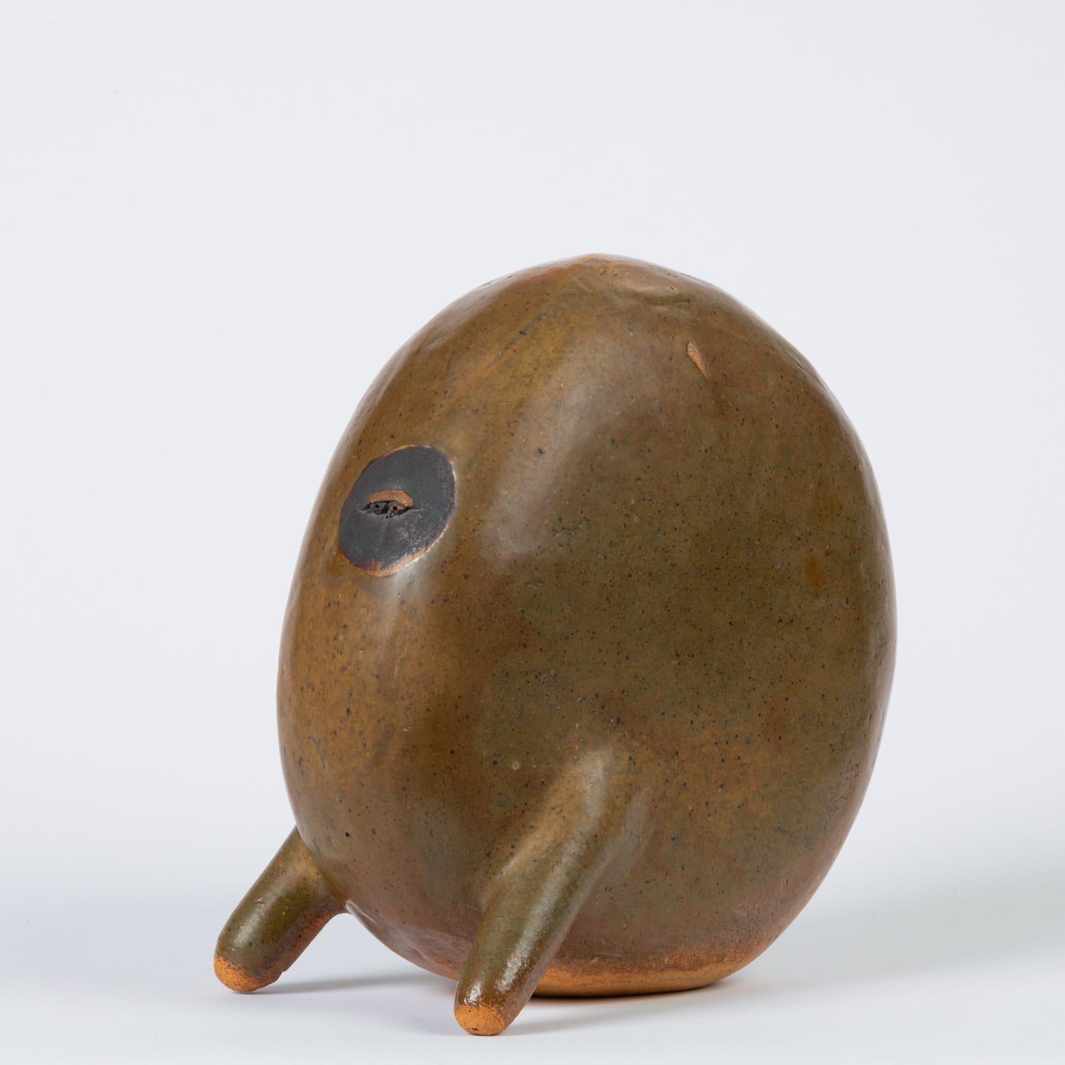 A fanciful example of midcentury Studio Pottery, this piece is a bipedal ovoid creature with a heavy brown. The Minimalist composition has a large body with an irregular glaze finish. A “face” is demarcated by a small circle of darker glaze, in