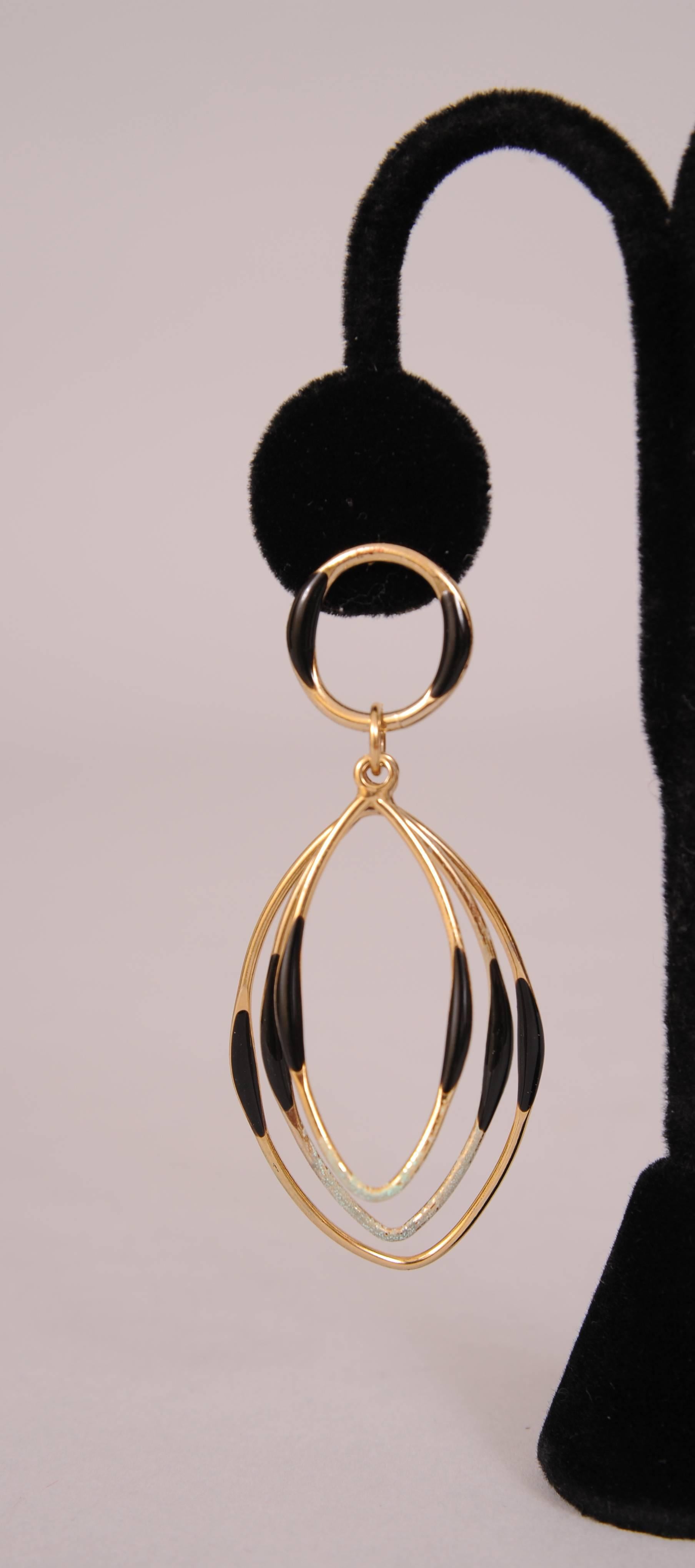 An unusual design makes this pair of 1970's pierced earrings very eye catching. The round hoop at the top supports three graduated oval hoops suspended by a ring. All of these pieces have black enamel decoration on the sides. Light weight and with
