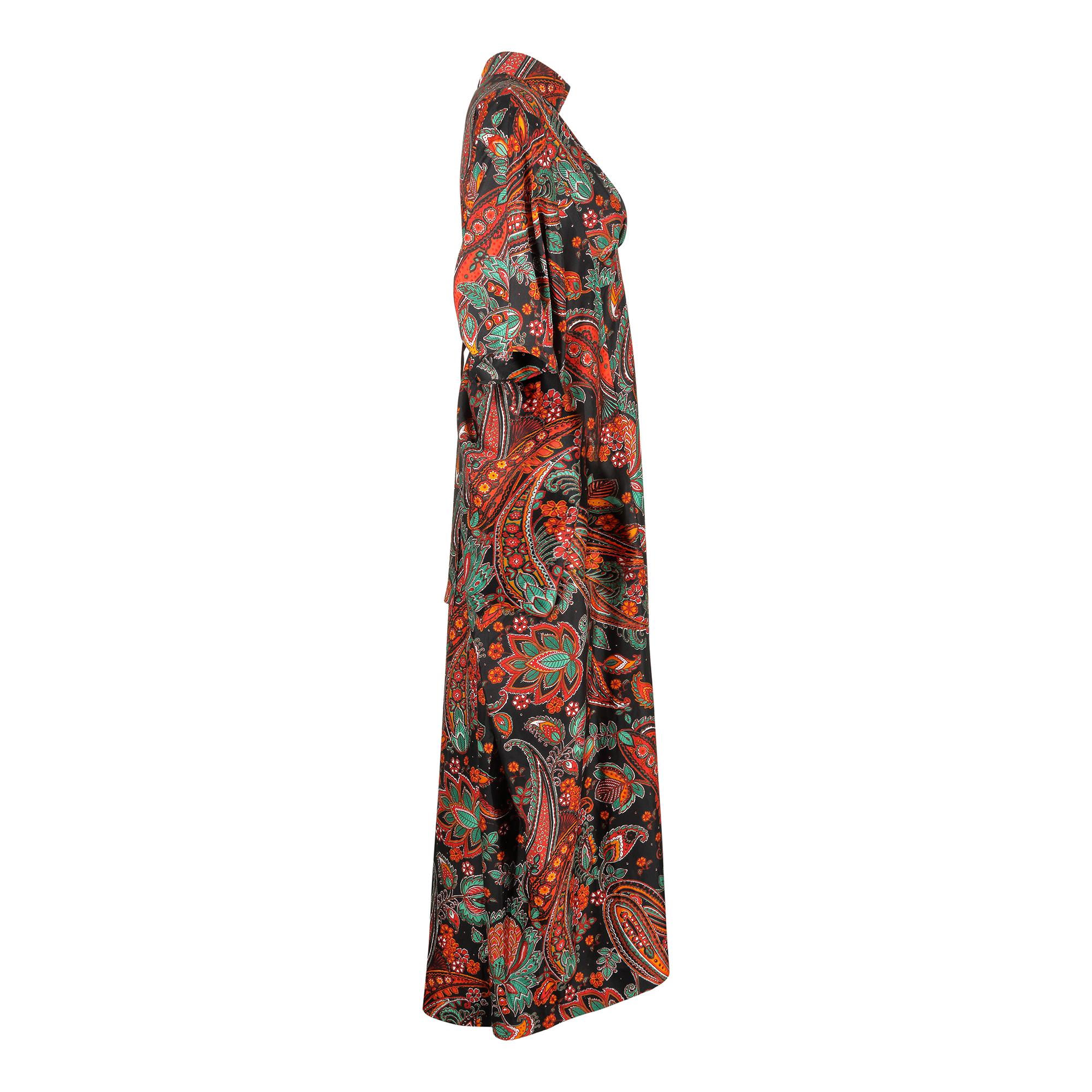A striking and original 1970s kaftan or trapeze style dress.  It has a brightly coloured floral Paisley pattern in red, orange, green and white tones against a black background. The fabric composition is not known but it feels like a good quality