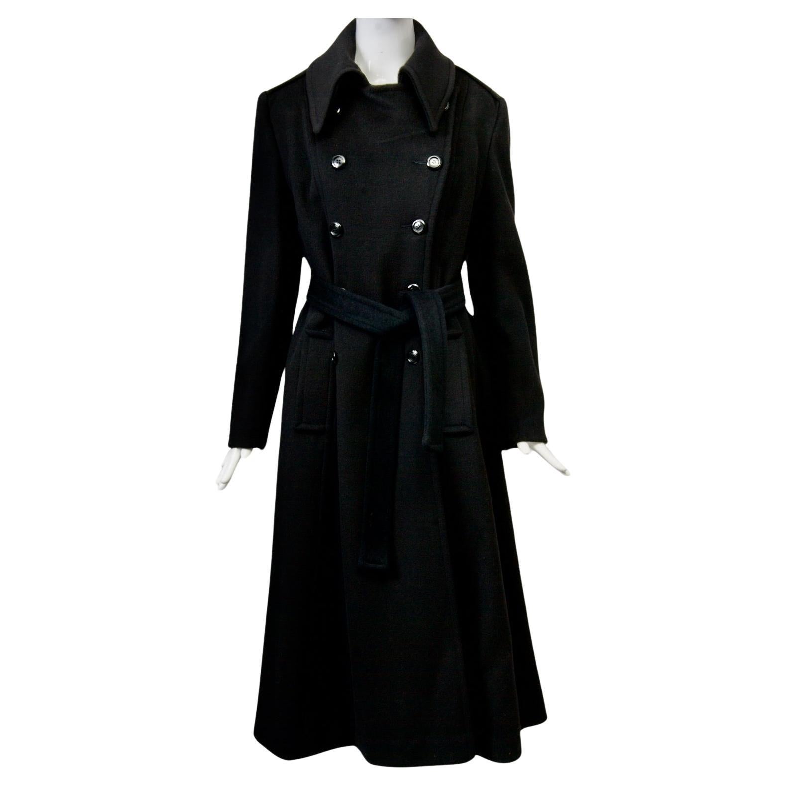 Black plush wool maxi coat features double-breasted styling and self sash. The coat buttons up to the pointed collar. Set-in sleeves with two buttons at each wrist and shoulder epaulets. Vertical bound pockets are positioned adjacent to welted seams