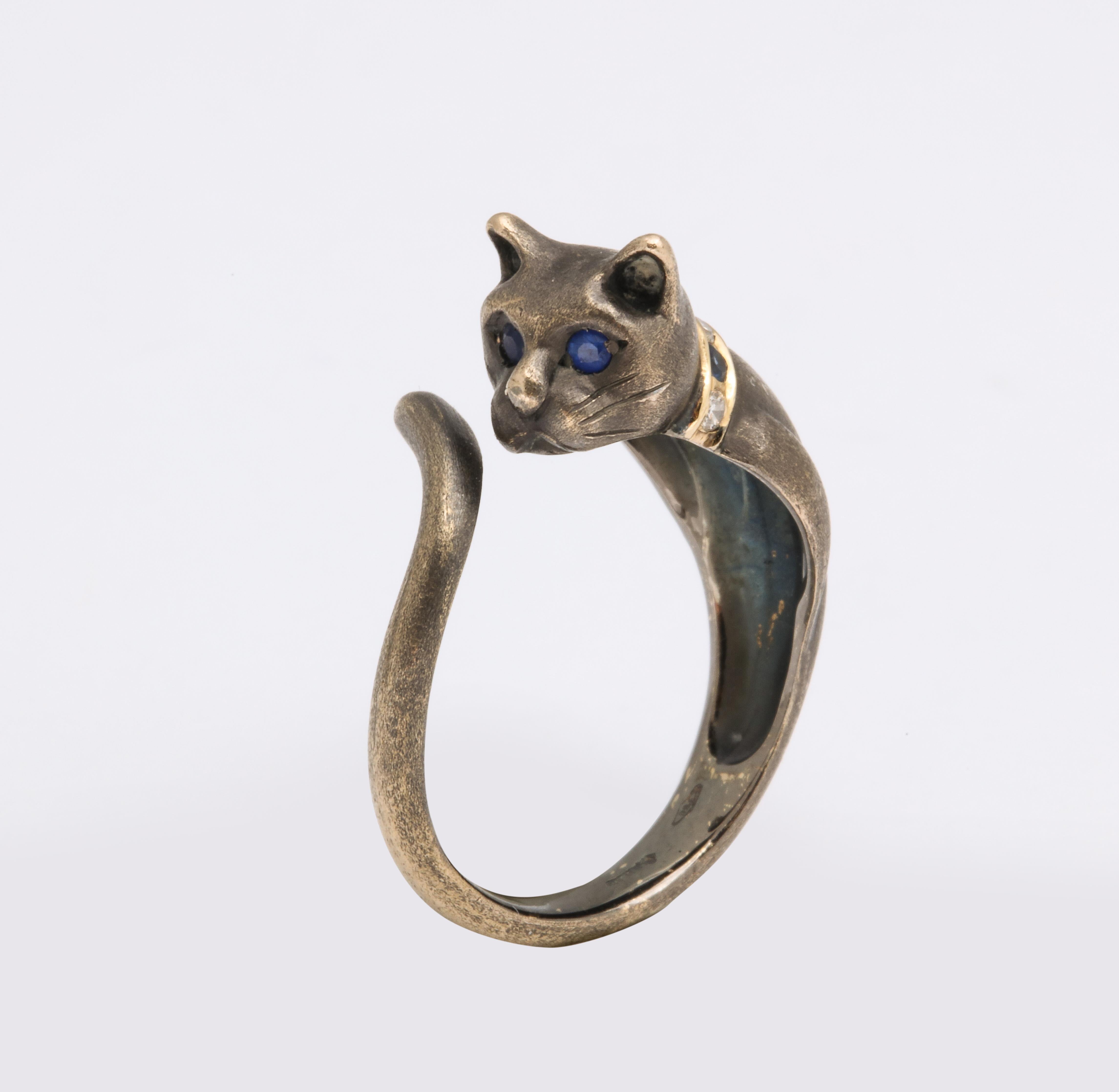 In the form of a lifelike cat of blackened 18k gold with sapphire eyes and engraved whiskers, its satin finish resembling cat fur, enhanced with a sapphire and diamond collar on polished gold. 

With French control mark, stamped 750, circa