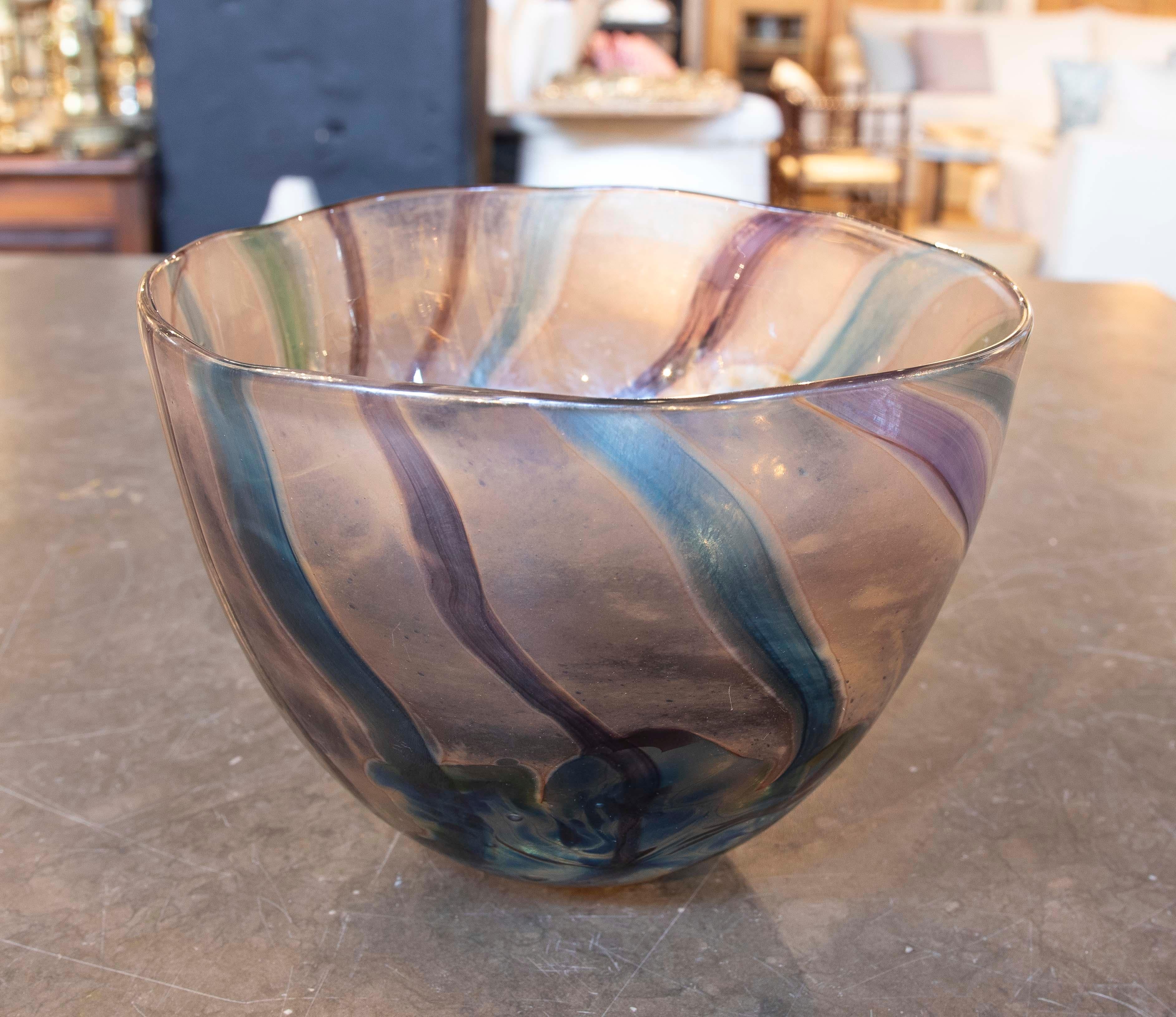 Beautiful handcrafted blown glass bowl, decorated with wavy lines in warm and cool tones that blend harmoniously. The piece features a unique design, characterized by its organic shape and translucent colors that add depth and visual