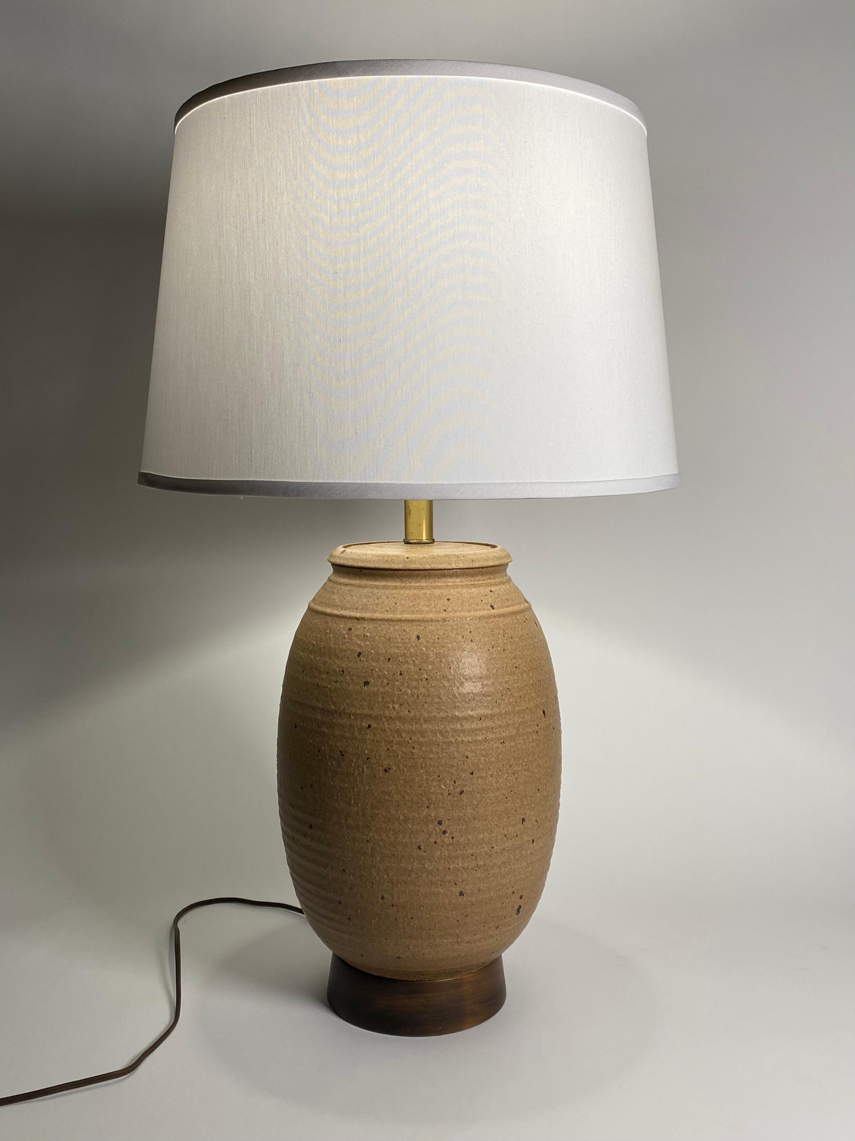Studio ceramic table lamp by Bob Kinzie for Affiliated Craftsman, having an earth tone brown body with dark brown speckles over the entire piece. Resting on a dark walnut colored wood base with brass hardware, measurements are a 9