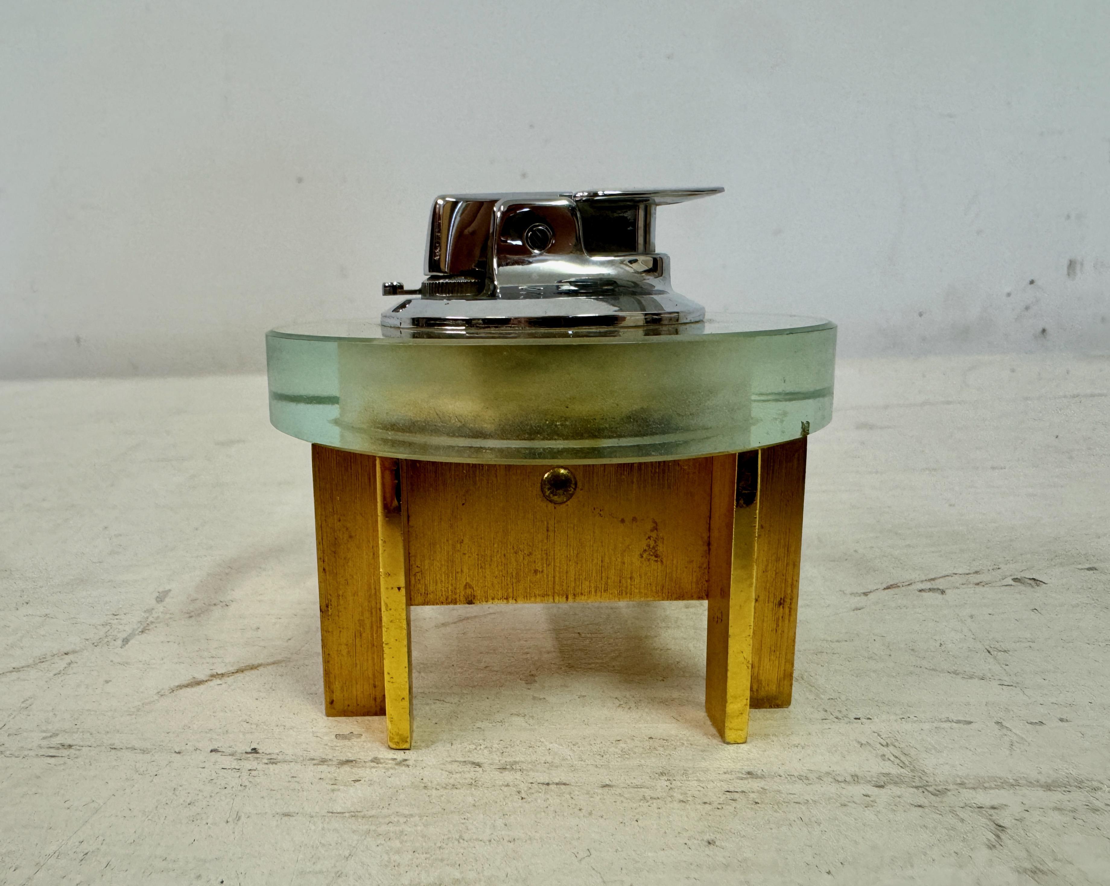 Desk Lighter 

By Ronson

Glass and gilt bronze or brass

1970s

There are a couple of very small nicks in the glass

This is a distinctive Ronson table lighter with a striking design that combines modernist and mid-century elements. The lighter is