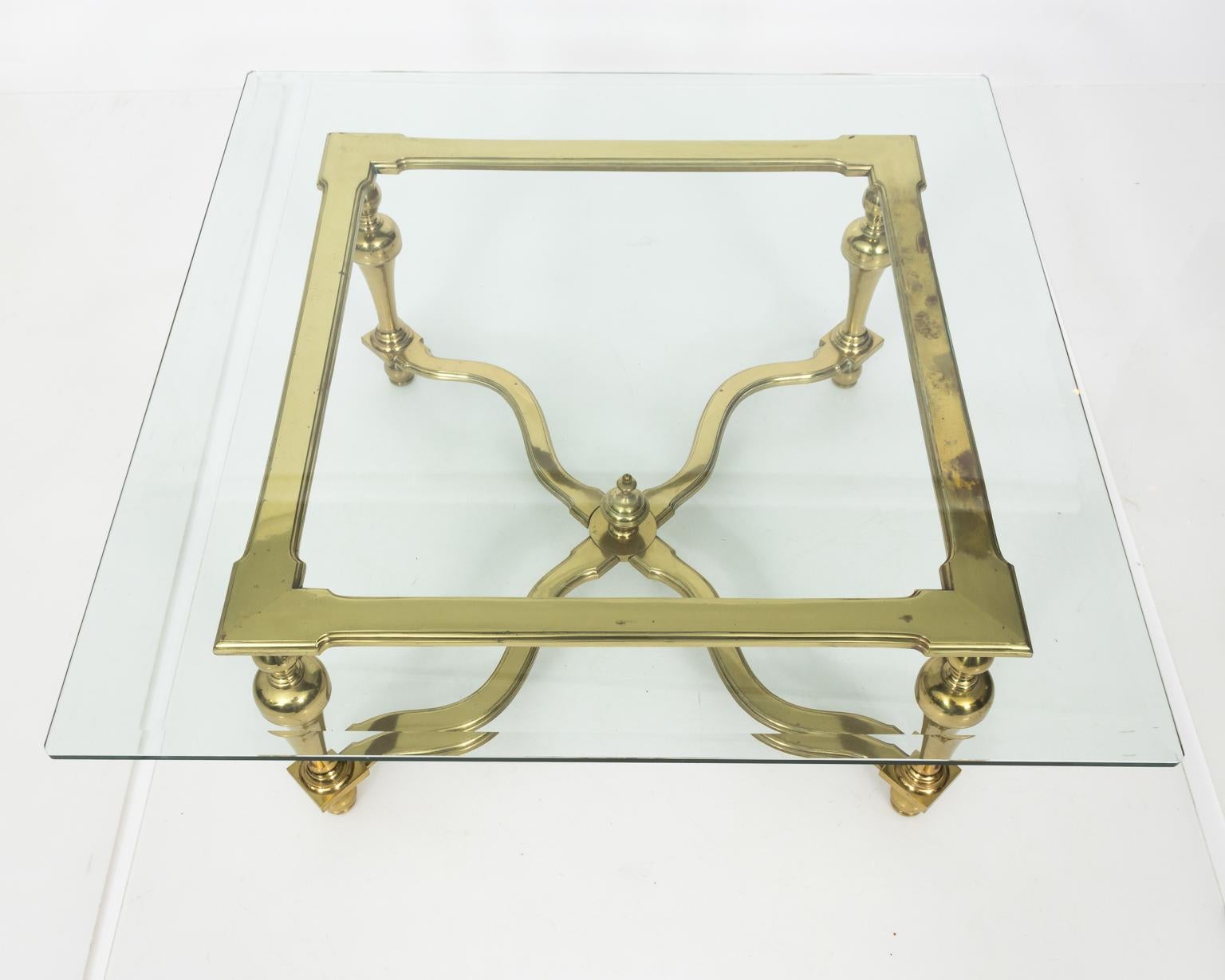 1970s brass and glass English coffee table with glass top. The base is highlighted by trumpet shaped legs and cross stretcher with a center ball finial.