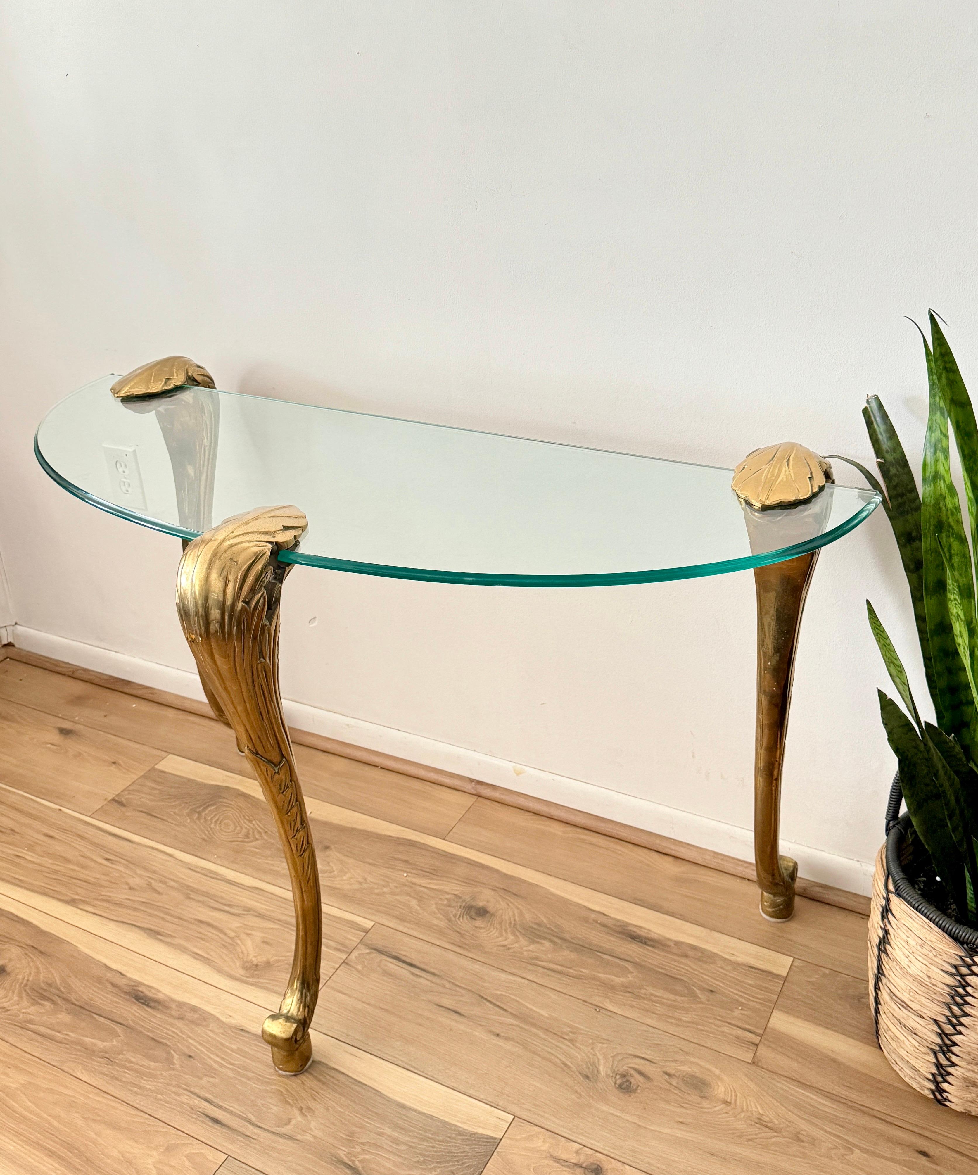 The console table consists of three heavy solid brass legs and a floating clear glass top.



