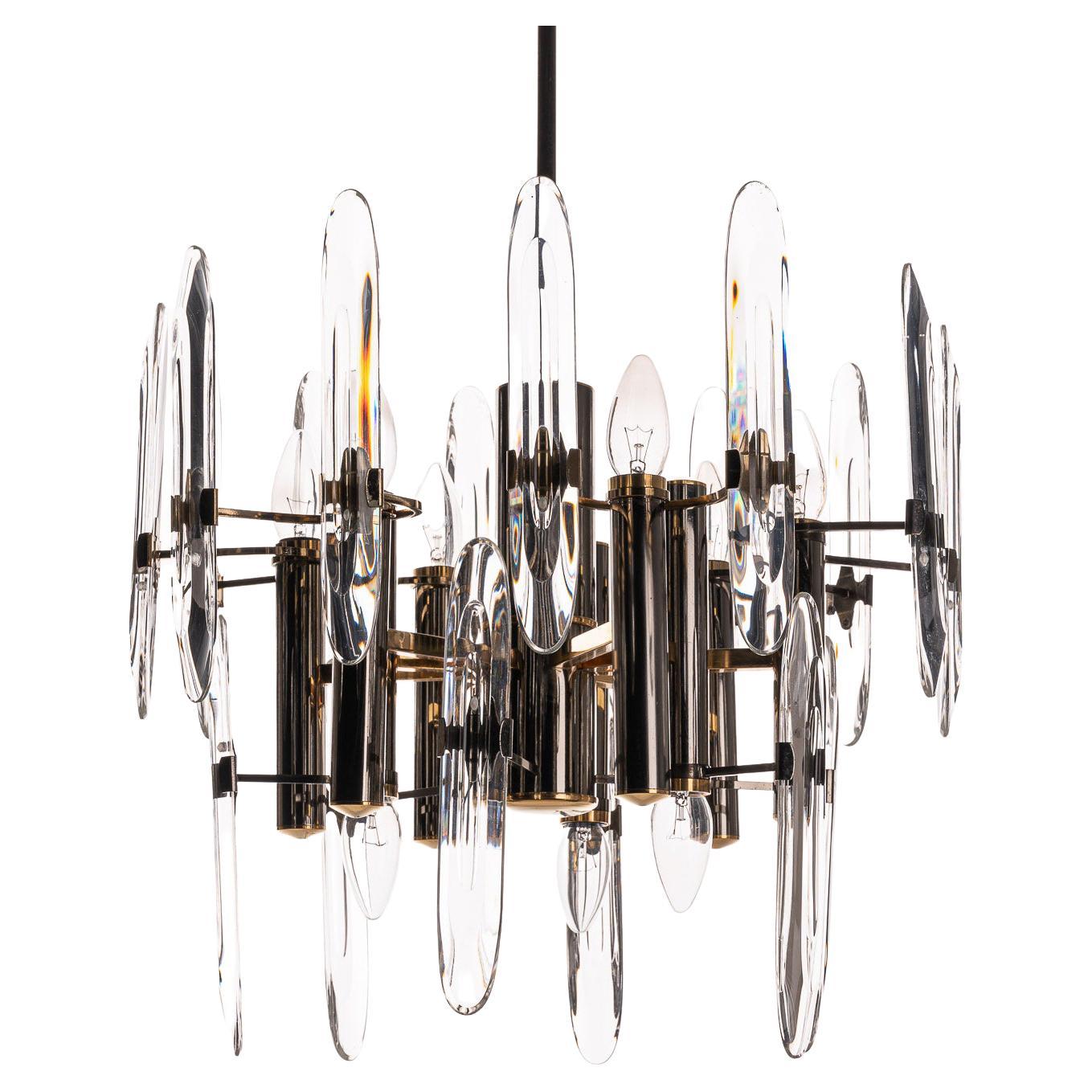 Classic 1970s Italian Gaetano Sciolari design chandelier with characteristic use of crystal glass and layered tiers of chrome and brass frame. It holds nine E14 lights of which three facing down.  