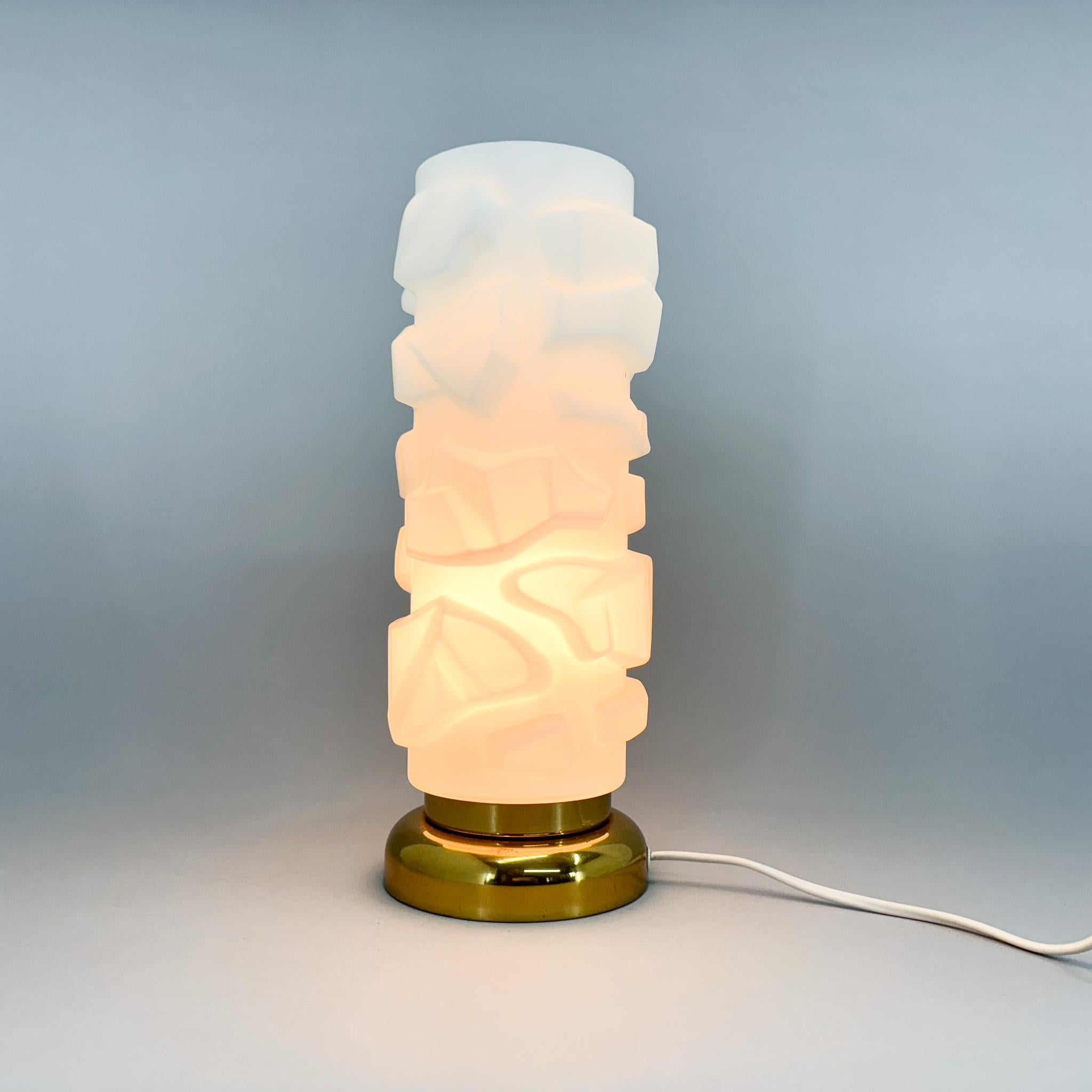 Vintage By  Lampe de table produite dans l'ancienne Tchécoslovaquie dans les années 1970. La lampe a une base en métal avec une finition en laiton et un abat-jour en verre opalin de forme géométrique inhabituelle. Ampoule 1 x E26 - E27. Adaptateur