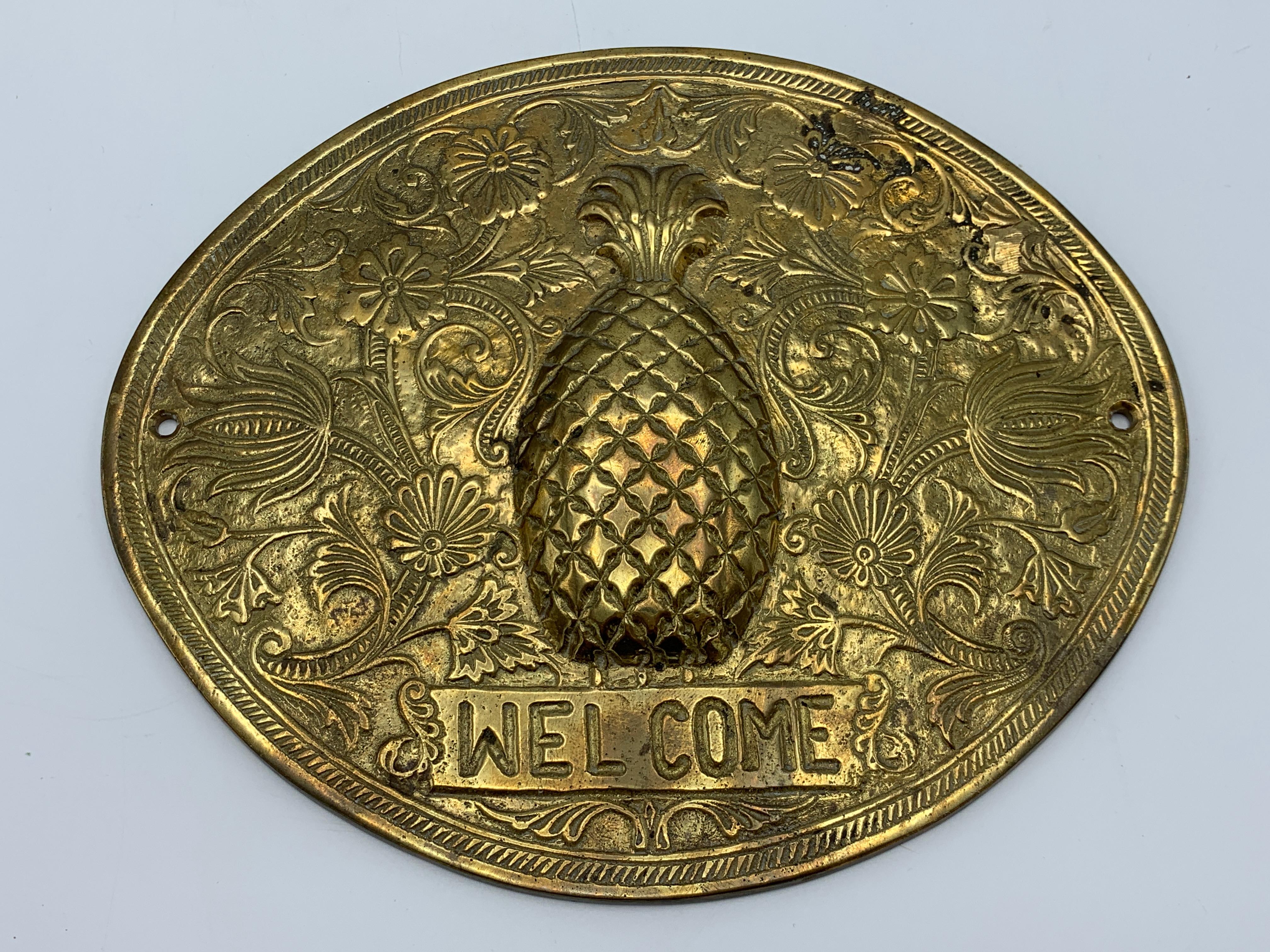 Listed is a gorgeous, 1970s solid-brass pineapple 'Welcome' wall plaque. Heavily detailed with a raised pineapple in the center, with floral motif surrounding as a border, and 'Welcome' stamped beneath. Heavy, weighing 1.5lbs. Includes brass screws.