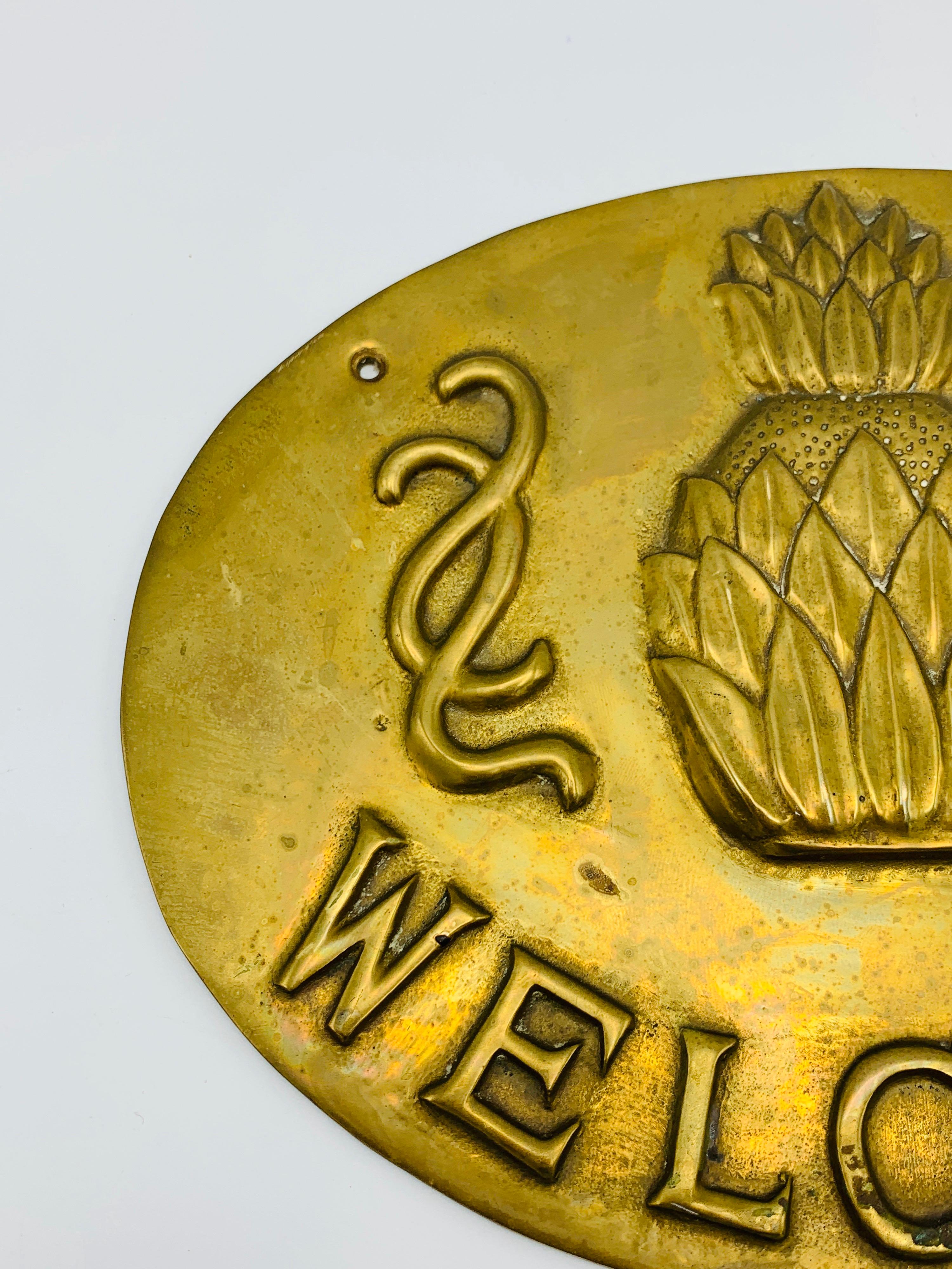 Listed is a beautiful, 1970s solid brass pineapple 'Welcome' wall plaque. Detailed with a raised pineapple in the center, with a floral motif surrounding, and below 'Welcome' stamped into the brass. Heavy, weighing 1.6lbs.