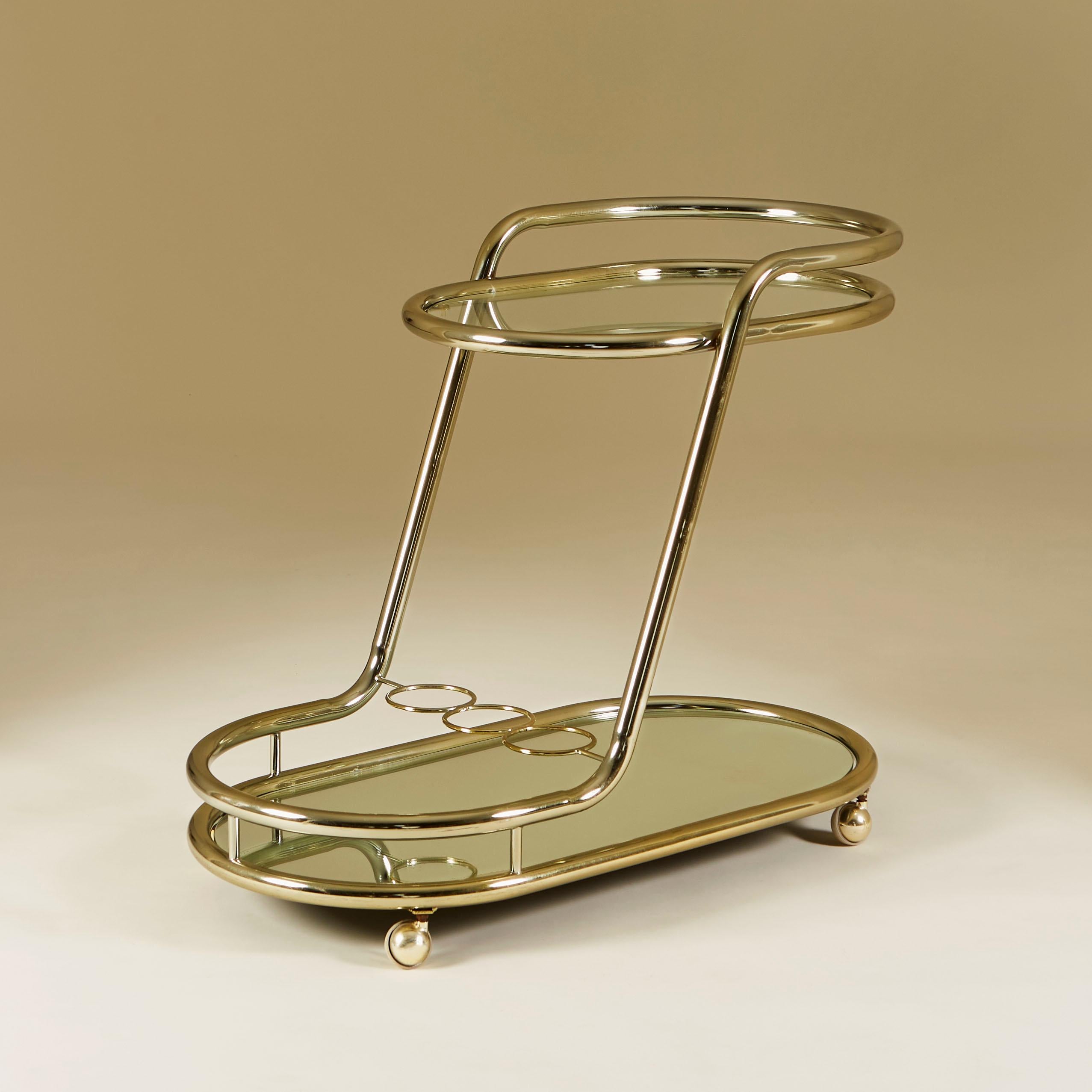 Chic pale golden brass trolley with simple tubular design to form decorative frame and handle. Gives the illusion of a floating top tier. Glass upper shelf and mirrored base shelf. Simple brass bottle holder for 3 bottles. Sits on golden castor