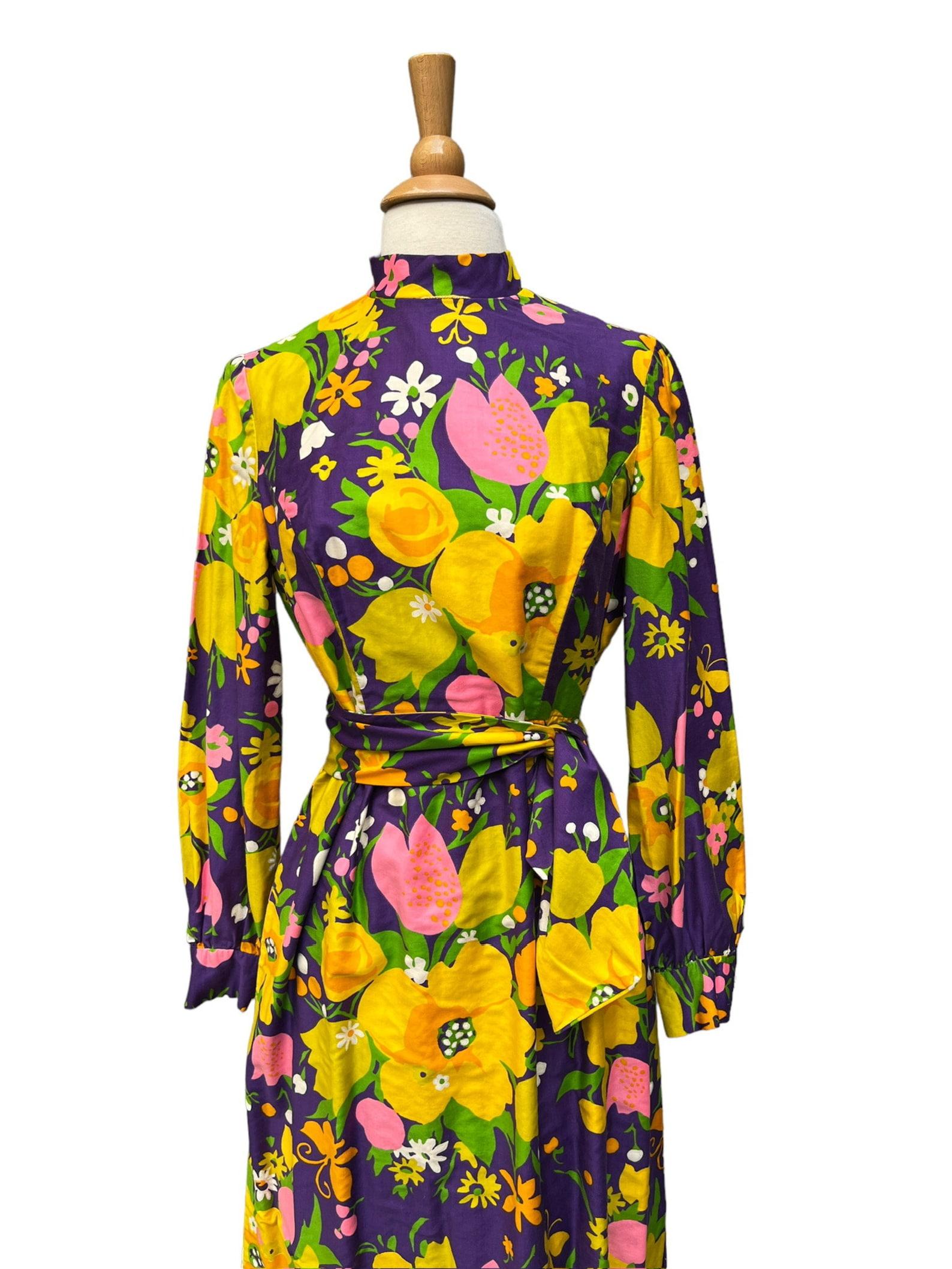 Brenner Couture maxi dress
large scale floral print
mock neck collar
long sleeves with button cuffs
matching self fabric belt
side slit hem on the left
back zip closure
has pockets
dress is lined
small yellow loop running along the collar so that