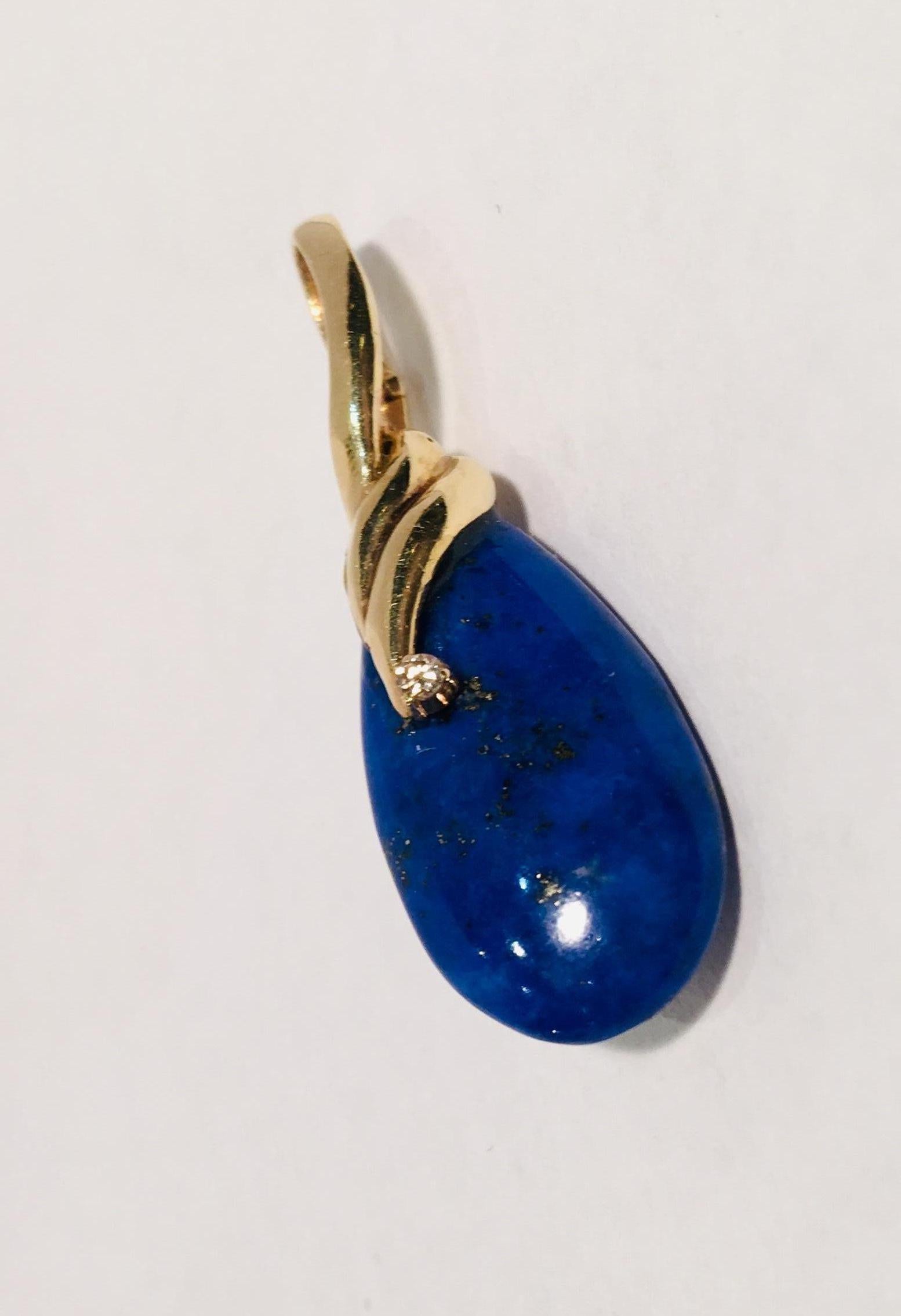 Lovely estate pendant features a teardrop or pear shaped, hand-cut, bright blue lapis lazuli stone, richly flecked with gold and suspended from the enhancer bale with a graceful swirl of 14 karat yellow gold and accented by a prong set round