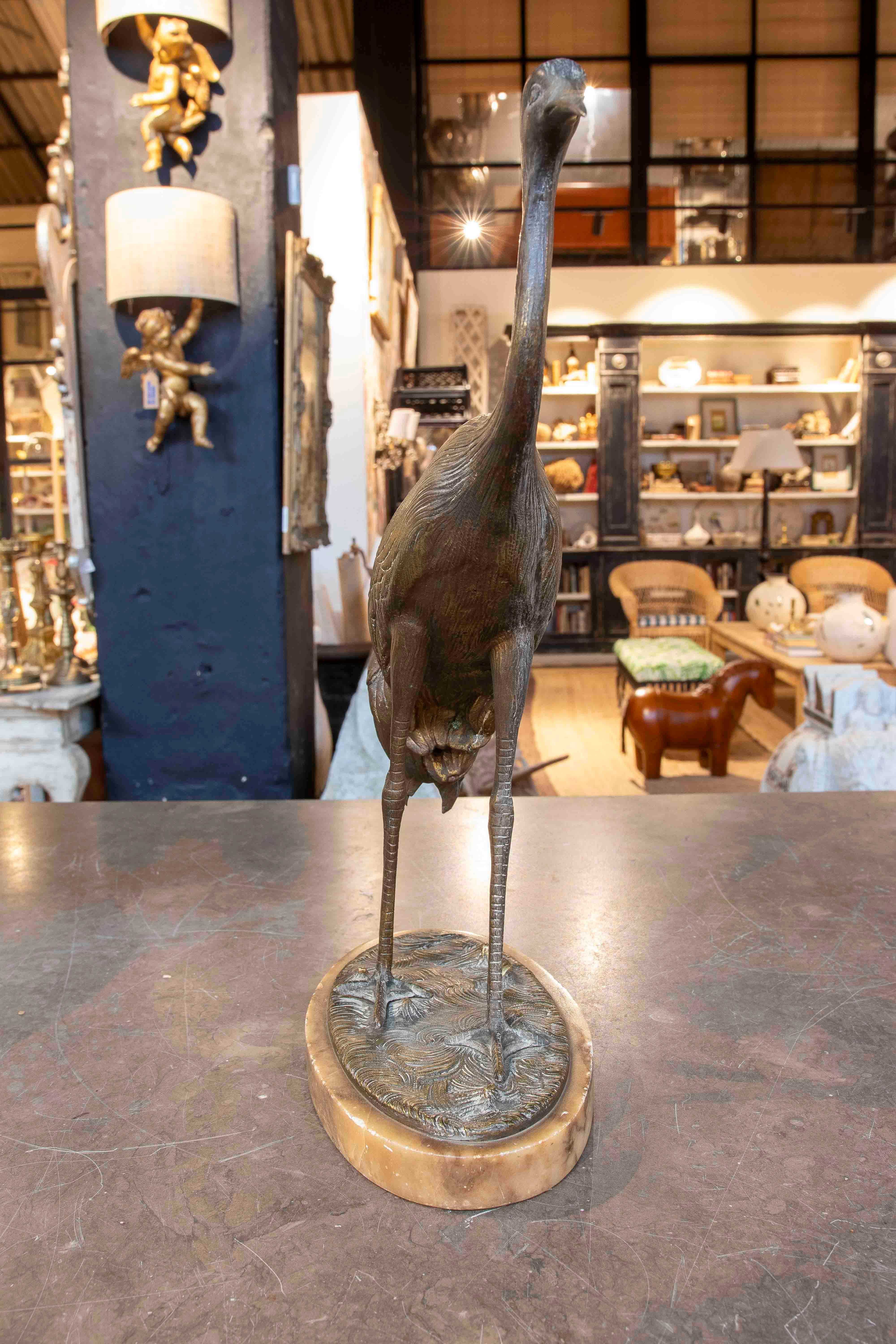 Une élégante sculpture de grue en bronze, rendue dans un design détaillé et réaliste qui met en valeur la grâce et la beauté naturelle de cet oiseau majestueux. La figure est élancée, avec son long cou courbé et sa posture sereine, évoquant le