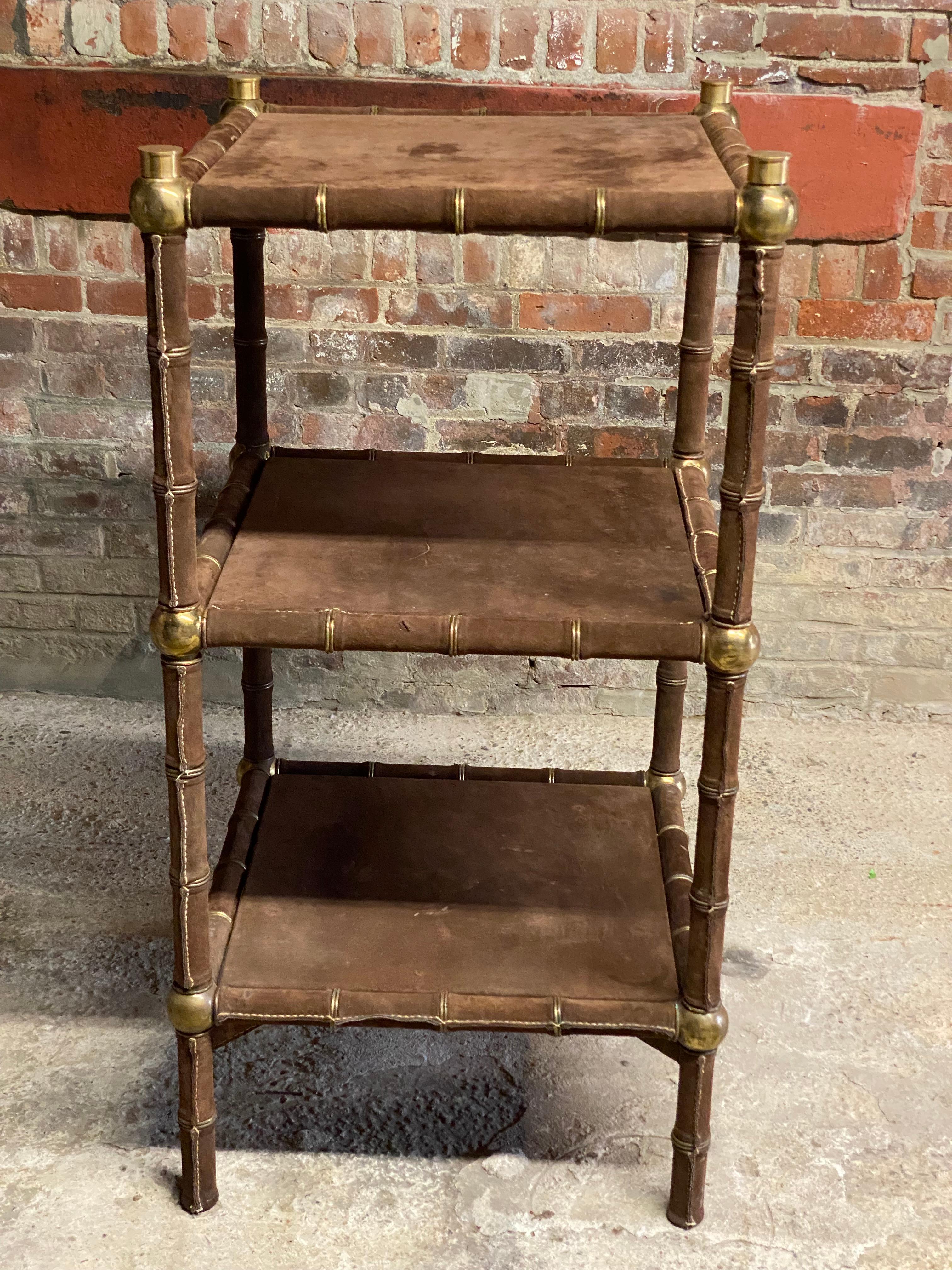 A spectacular three tiered suede and brass shelving unit. Wrapped brown suede (Nubuck?) shelves with brass caps and rings. Circa 1975. This Post-Modern style is reminiscent of great clothing designers of the 1970s producing some fantastic decorative