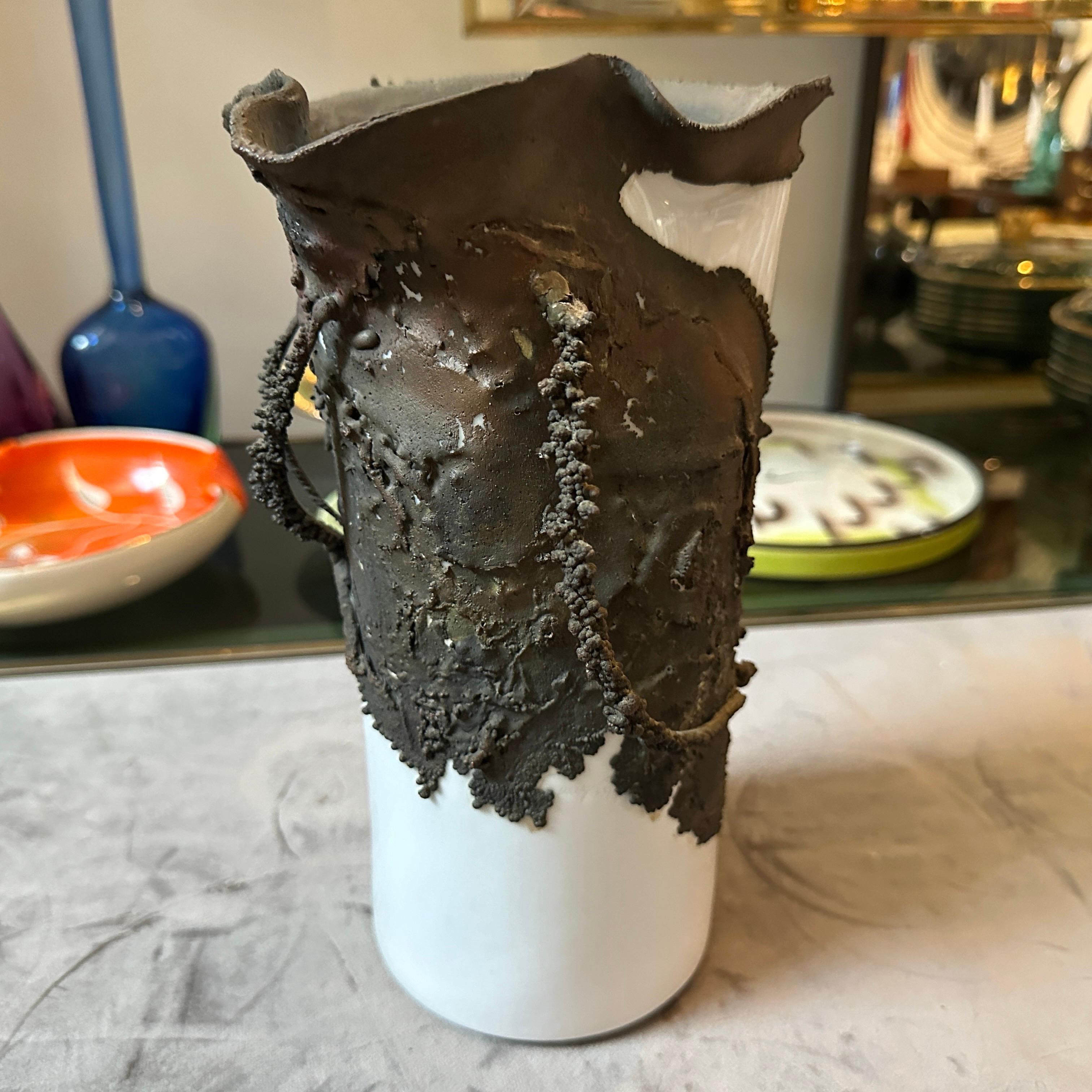 Questo vaso scultura brutalista degli anni '70 combina bronzo e porcellana bianca in un design sorprendente e contrastante tipico dell'estetica brutalista. La base del vaso è realizzata in porcellana bianca liscia e lucida, che forma una semplice