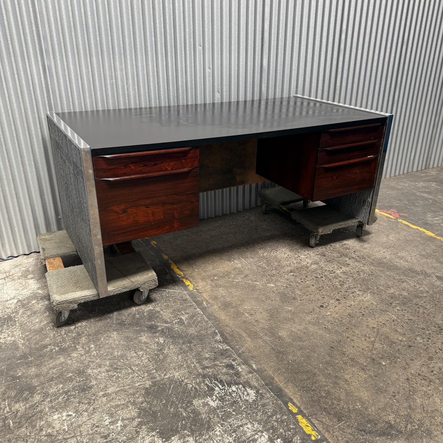 AMBIANIC presents
1970s Stunning Executive Desk by Billy Joe Mccarroll & David Gillespie
Forms + Surfaces Inc Santa Barbara, California.
Fabulous Black Formica Top Brutalist Steel coverings 
Rosewood drawers with sculptural built-in handles.
Lock