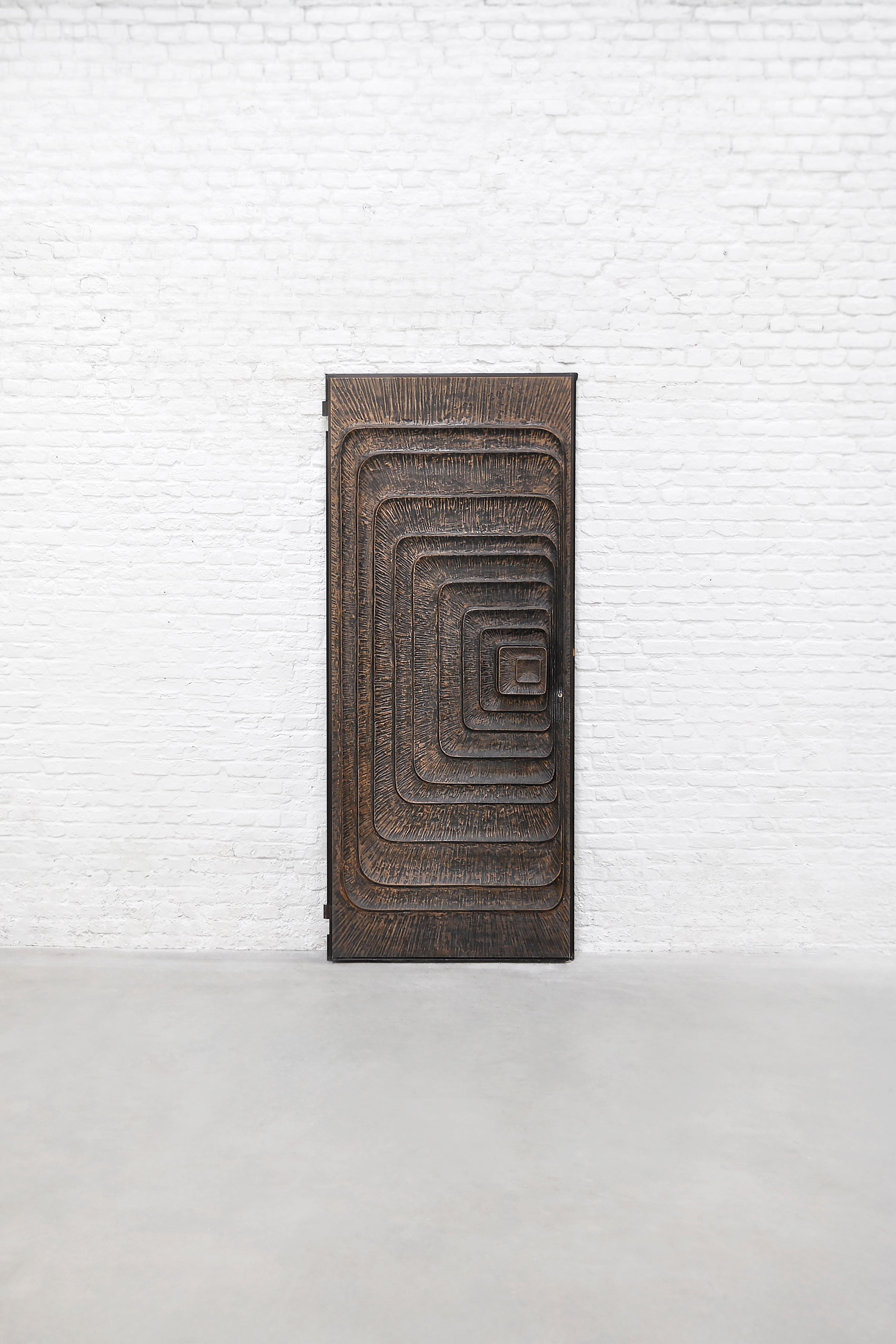 A striking and unique 1970s Brutalist sculptural door, crafted in textured metal with a dynamic geometric relief pattern. This exceptional piece embodies the raw, expressive aesthetics of Brutalism, featuring a series of deeply carved, concentric