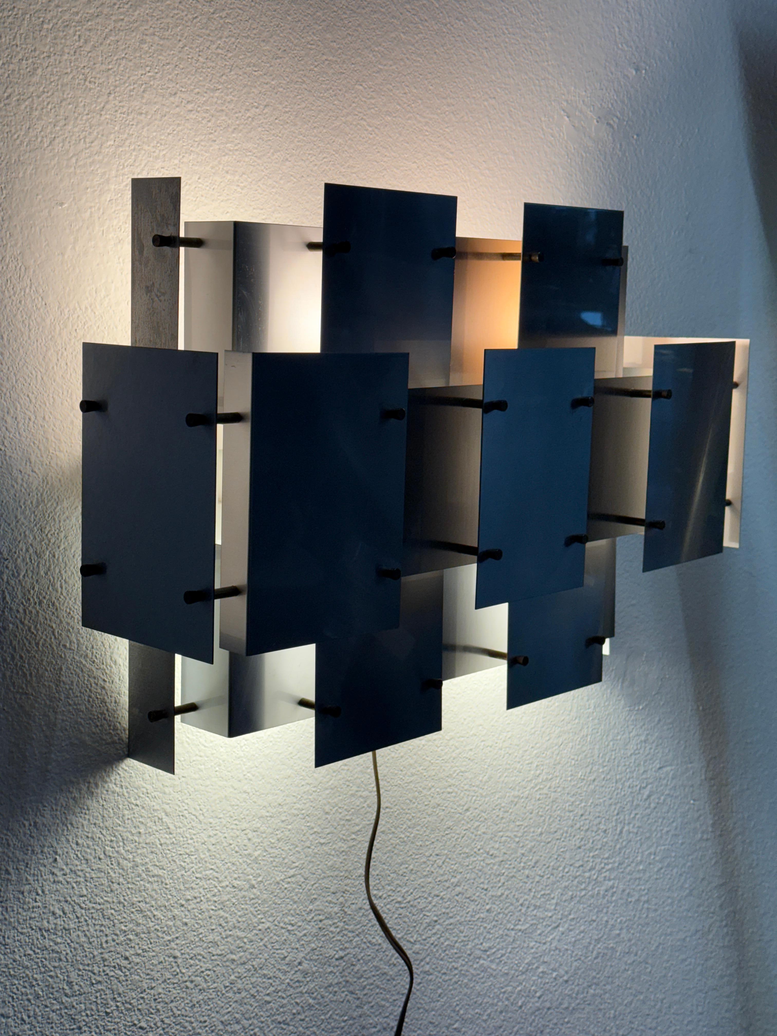 A nice Brutalist 1970’s Sonneman Lighting Cityscape sconce. It is in working condition. One interior panel has masking tape or paper on the interior of a panel giving it a softer glow. There steel piece has some marks, bends and imperfections,