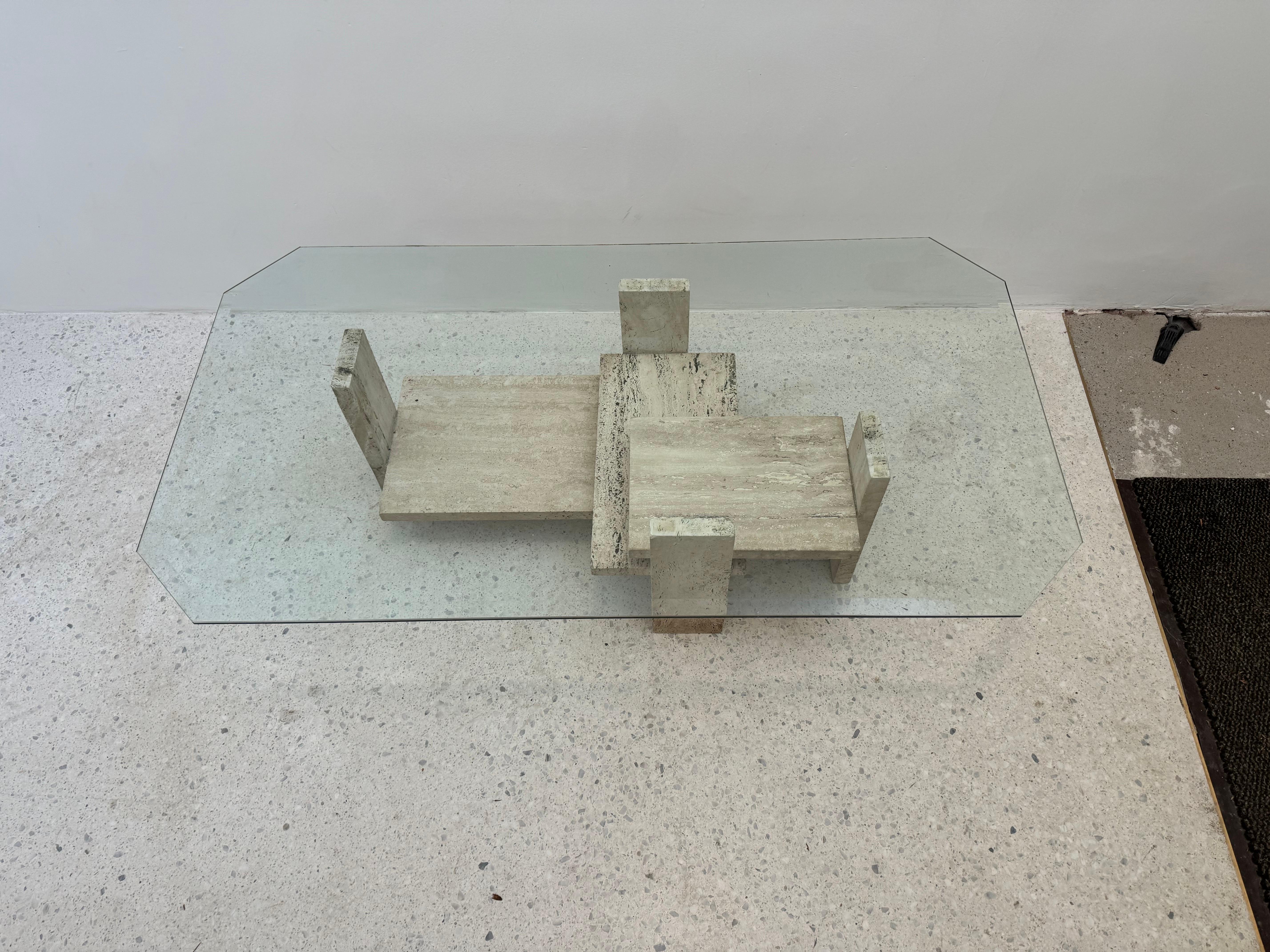 Elegant travertine and glass coffee table by Belgian designer Willy Ballez, created in the 1970s. This sculptural piece features an architectural travertine base composed of interlocking geometric blocks supporting a thick, beveled glass top. The