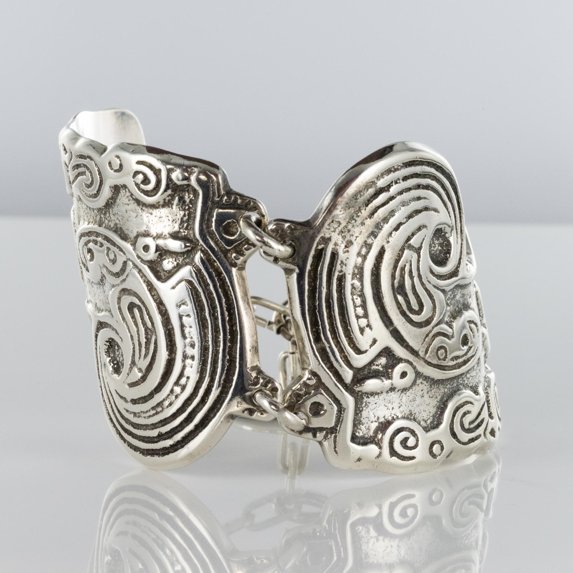 Bracelet in silver plated.
Large modernist bracelet, it consists of 2 curved plates interconnected by solid silver plated rings. Each plate has a modernist engraved decoration. The silver plated bracelet closes with a chain with spring ring and has