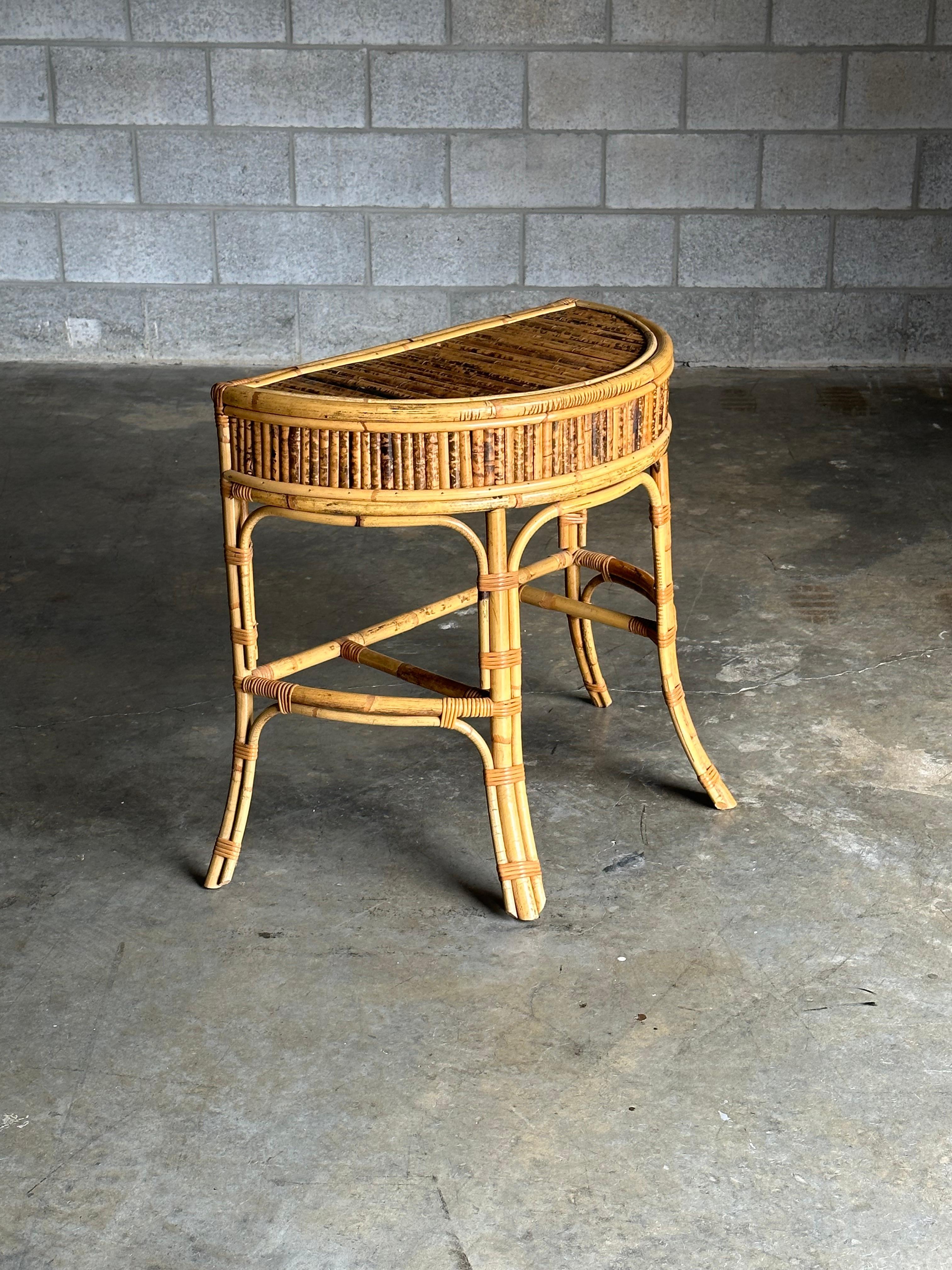 A wonderful small Demi-lune shaped console table. Executed in burnt bamboo with cane wrapping at the joints. This is a wonderful size that could be used in a variety of applications. 

Would work well in coastal, boho-chic, mid century, and