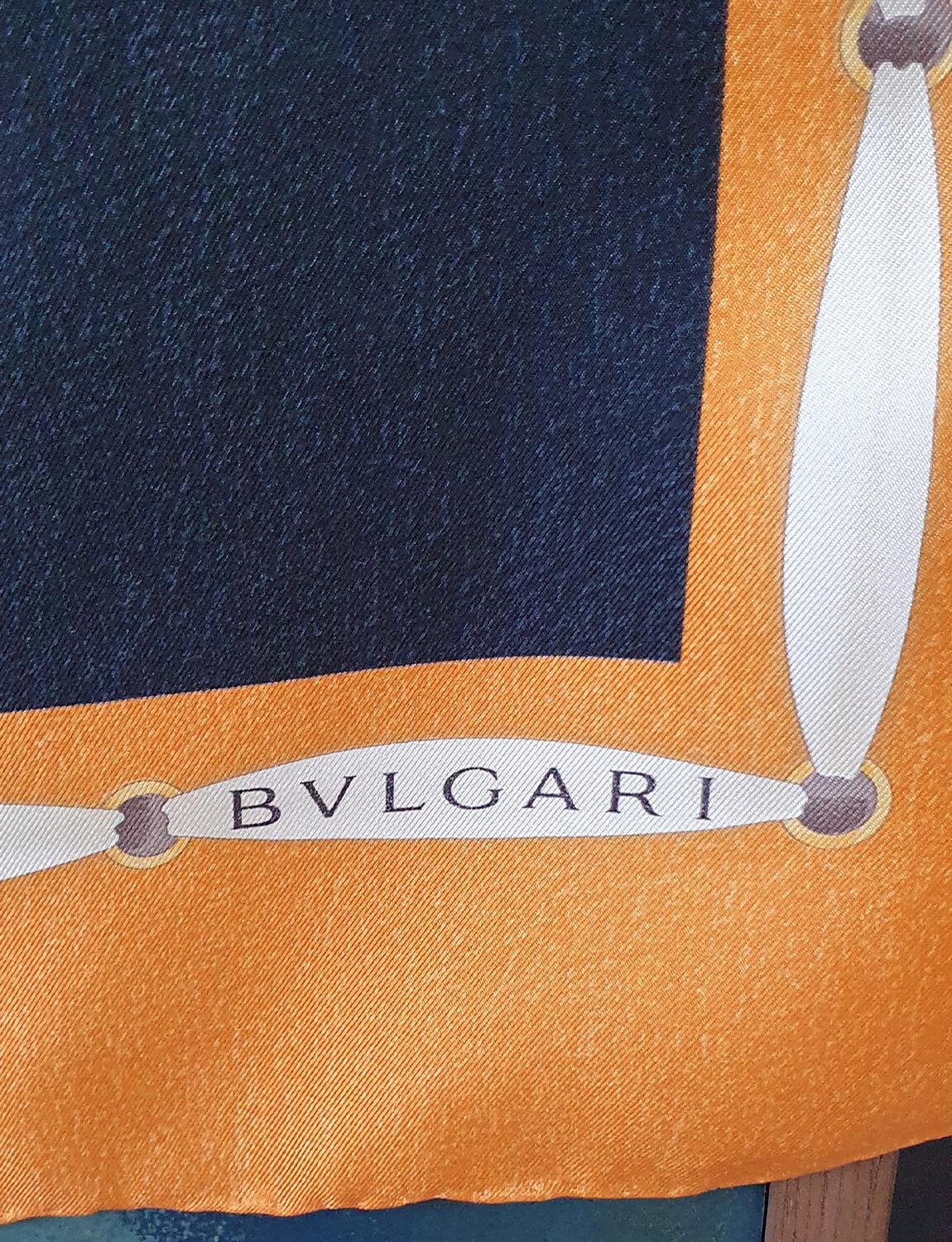 A beautifully designed vintage Bvlgari scarf with an orange border and navy centre silk centre. With lanterns, vases, handbags and objets as motifs in a variety of colours.  The foulard/scarf is signed by Davide Pizzigom and has the original Bvlgari