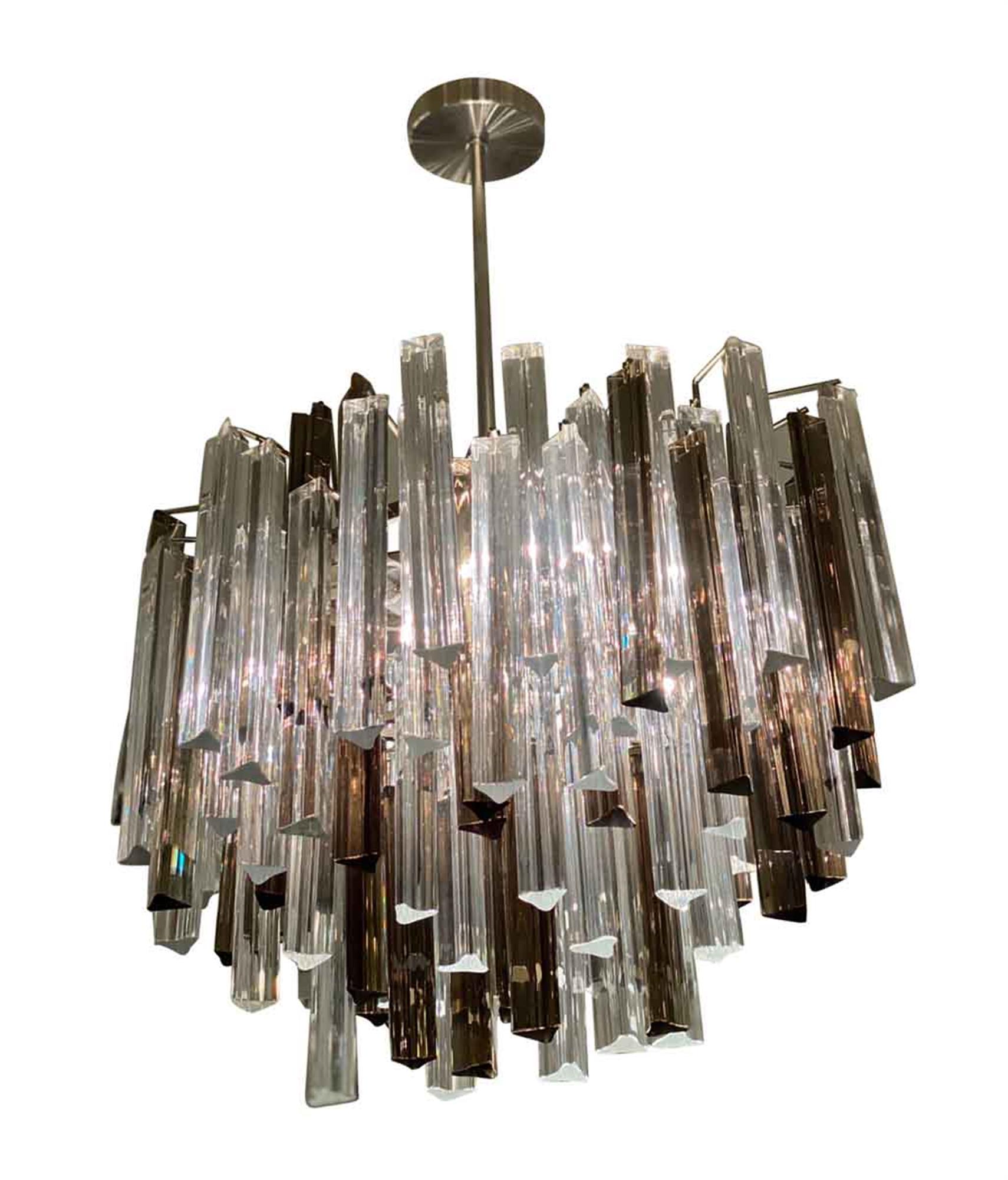 Offered is a 1970s Camer glass chandelier by Venini. This midcentury chandelier has both clear and smoked glass prisms, which are arranged in various levels to add to its prism light display. The canopy and pole are nickel. This is designed in an