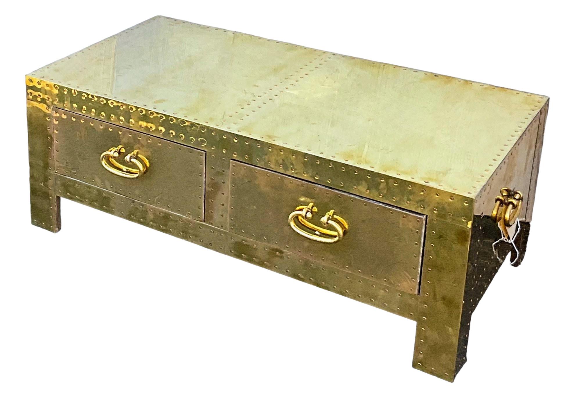 This is a campaign style brass clad trunk or coffee table by Sarreid Ltd. It has two drawers and nailhead trim throughout the body. It is a 1970s piece manufactured in Spain. It does have general wear throughout the piece.

My shipping can take two