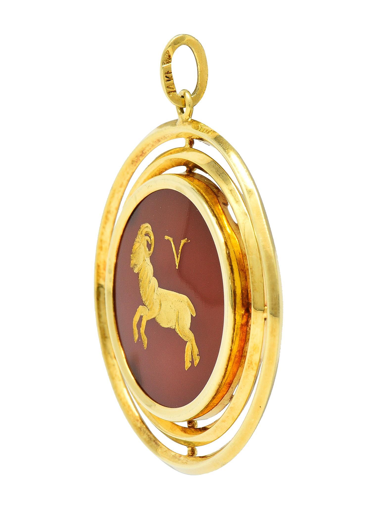 Designed as a round disk-shaped form centering a 20.0 mm round tablet of carnelian 
Translucent medium reddish-orange in color and centering an intaglio carving
Depicting a ram and the astrological symbol for Aries - filled with gold paint
Bezel set