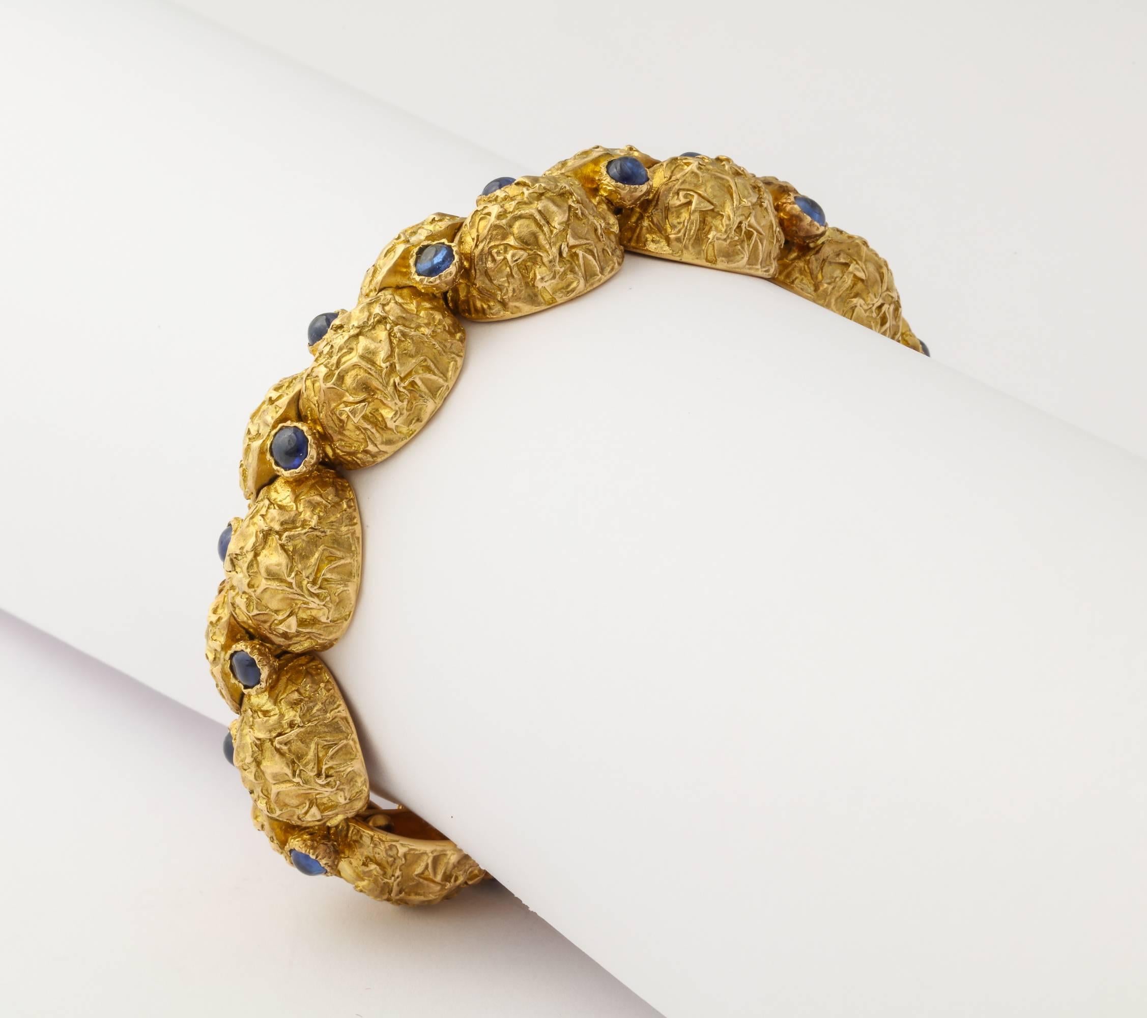 A modern and unusual 1970s bracelet from Cartier-Paris with deeply textured finish on quarter round segments of 18K gold each set with a cabochon sapphire and hinged to move independently and comfortably around the wrist. Measuring 7 1/2 inches